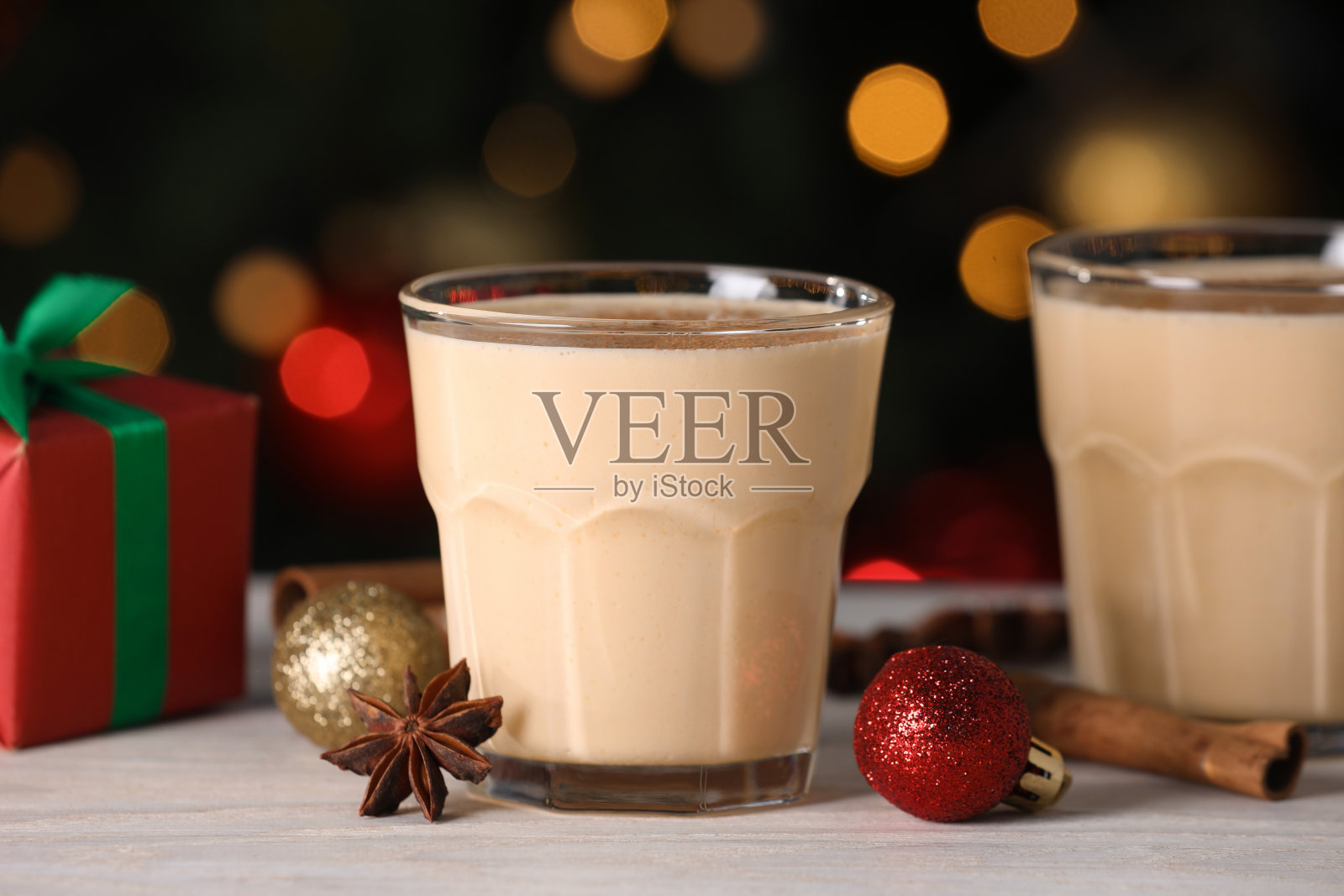 白色木桌上美味的蛋奶酒、肉桂、八角和圣诞装饰品映衬着模糊的灯光照片摄影图片