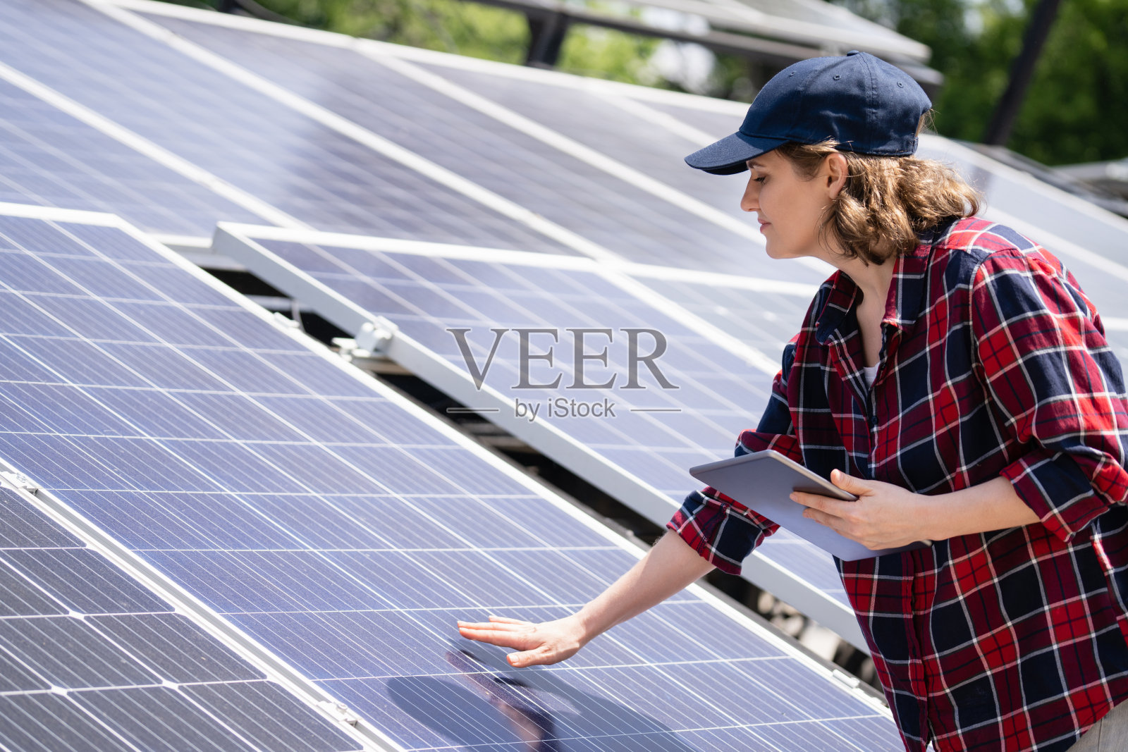 一位女工程师站在太阳能电池板旁边，手里拿着数码平板电脑。照片摄影图片