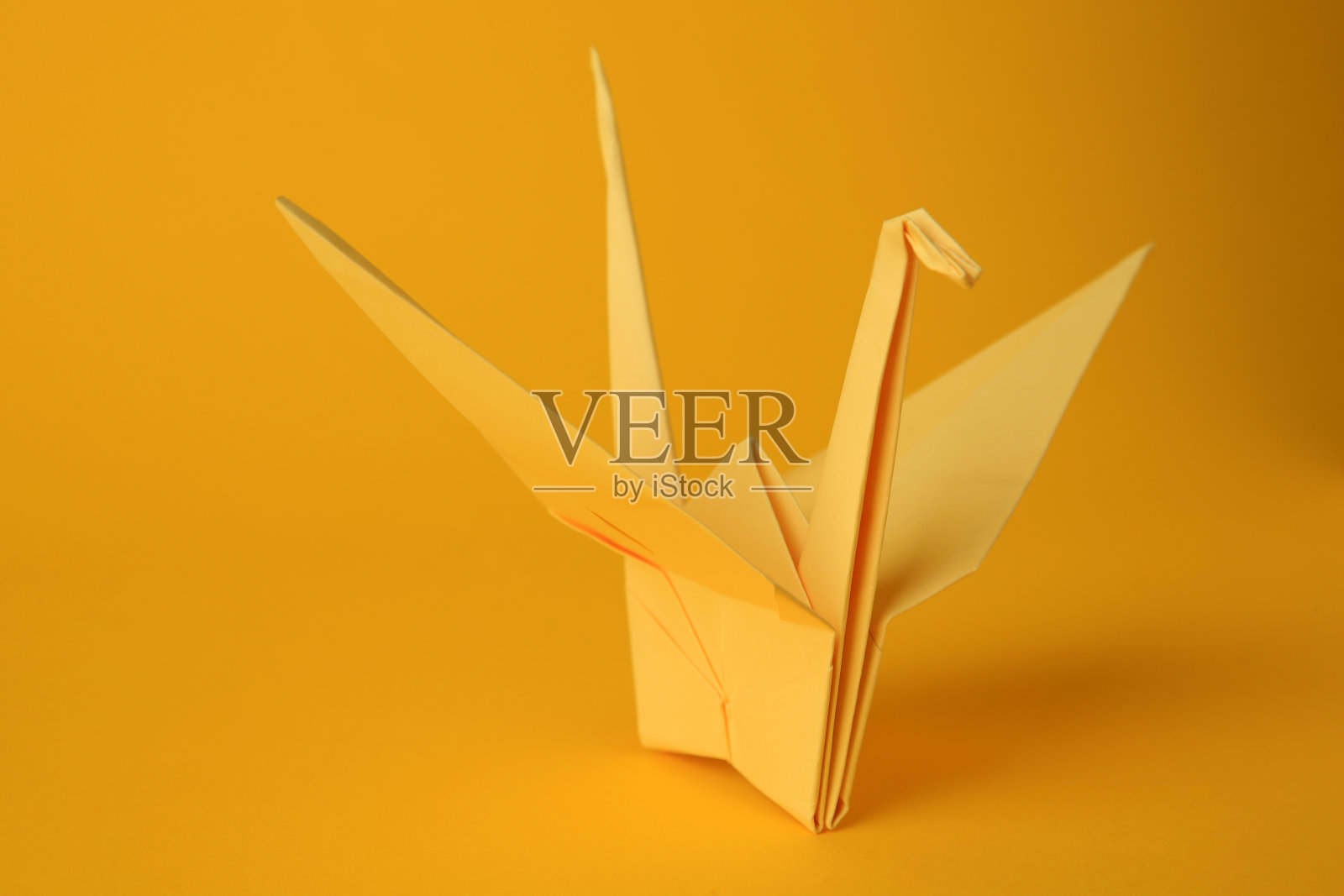 折纸艺术。美丽的淡黄色纸鹤在橙色的背景照片摄影图片