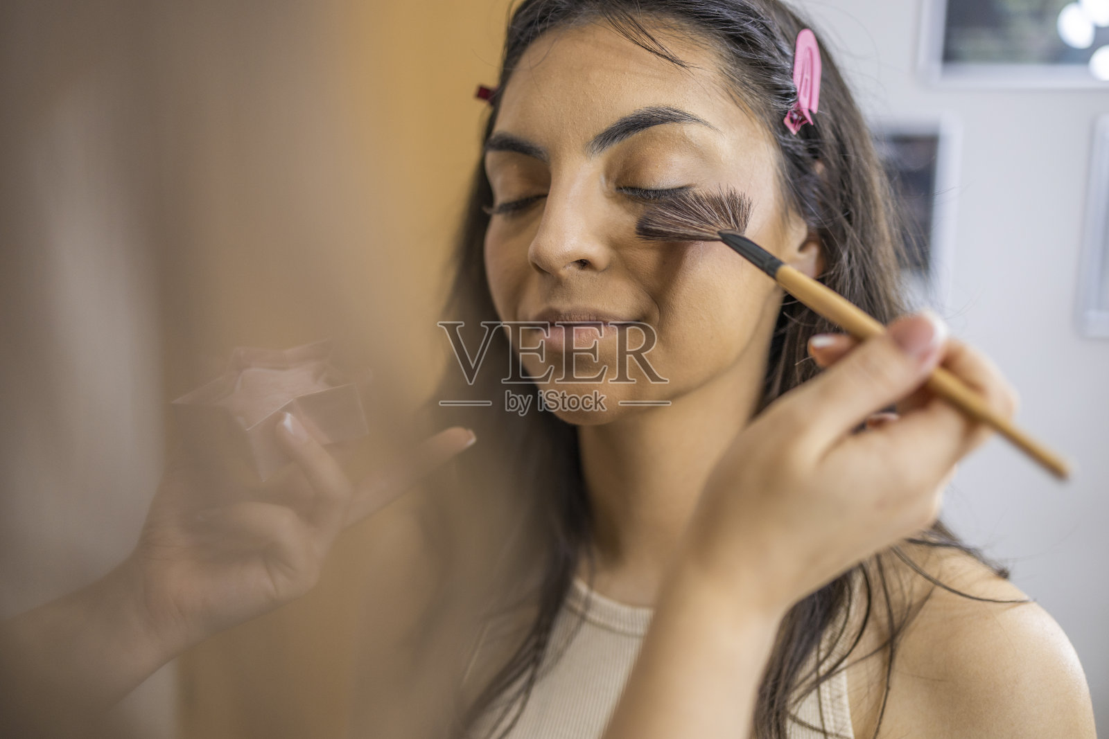 化妆师用高光笔在这个美丽的女孩身上涂上腮红。照片摄影图片