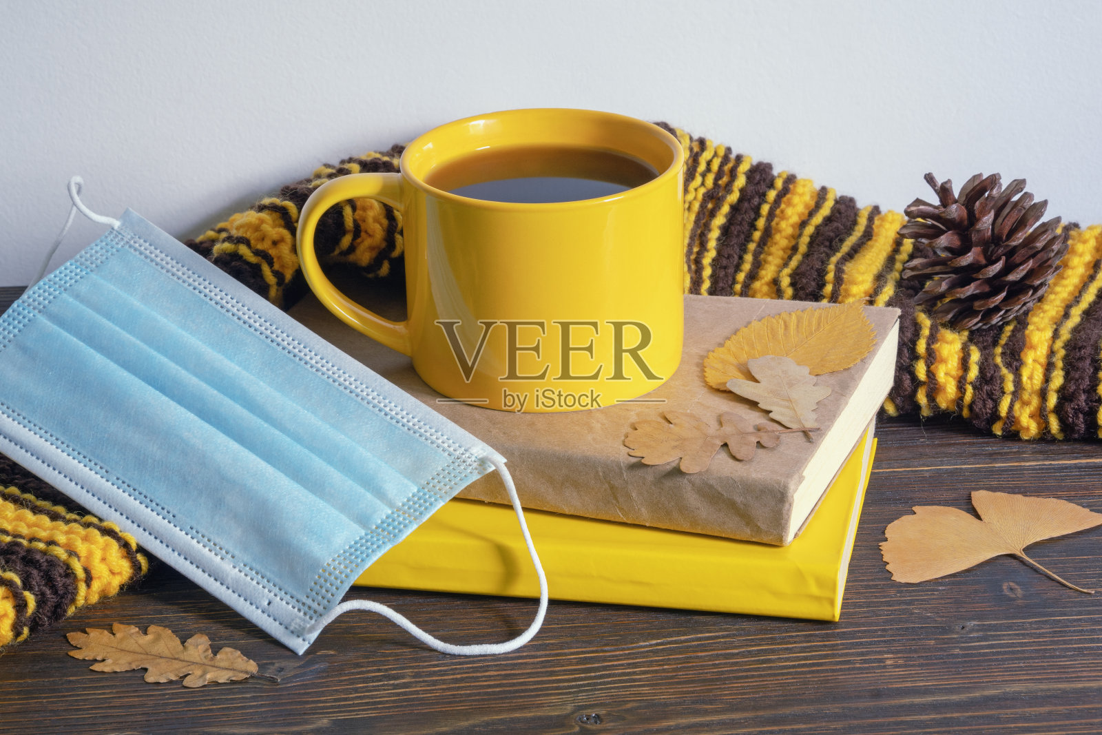 秋天。质朴的桌子上放着书、暖和的围巾、黄树叶、一杯咖啡和面罩照片摄影图片
