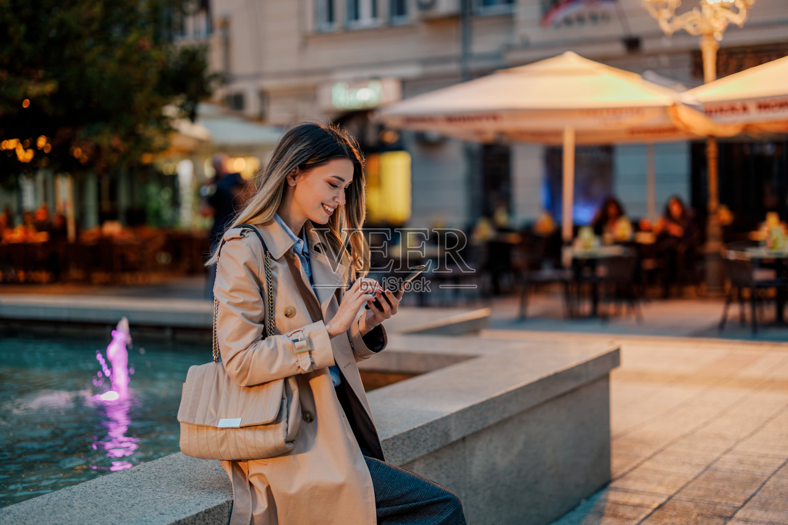 时尚女子坐在喷泉墙上用智能手机打字照片摄影图片