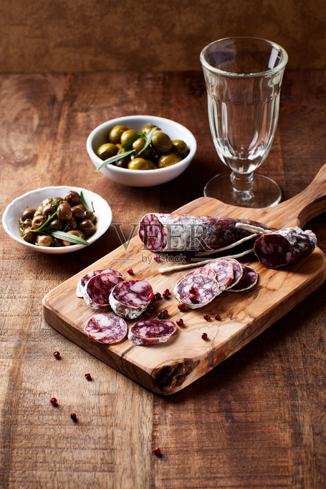 切片的法国腊肠配上新鲜的迷迭香和橄榄，质朴的木制背景。照片摄影图片