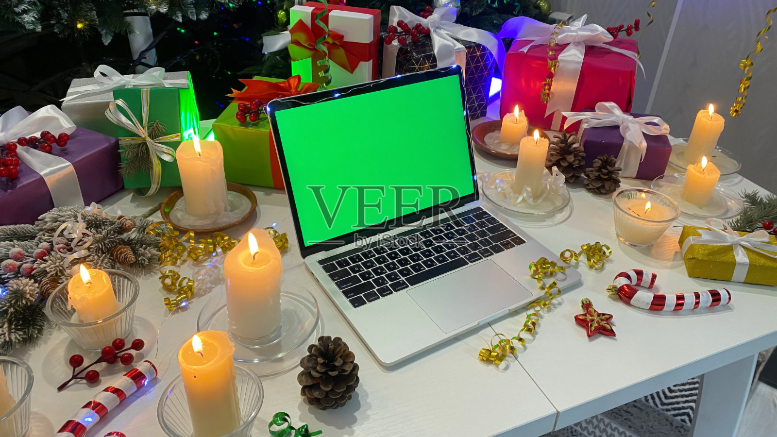 惊人的新年背景。新年桌上的一个远程工作者。屏幕上有色度键的个人笔记本电脑。明亮的礼品盒，点燃的蜡烛，甜筒，五彩纸屑照片摄影图片