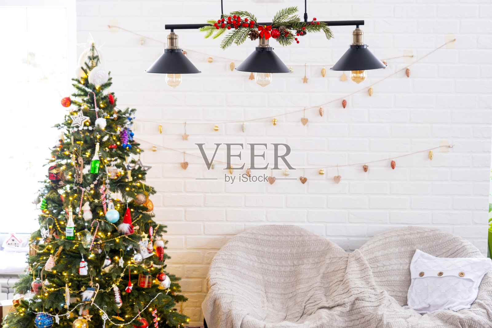 一棵白色的圣诞树，房子内部有阁楼式的砖墙，绳子上挂着玻璃玩具花环。发光的仙女灯装饰工作室的房间。温馨的家在圣诞和新年照片摄影图片