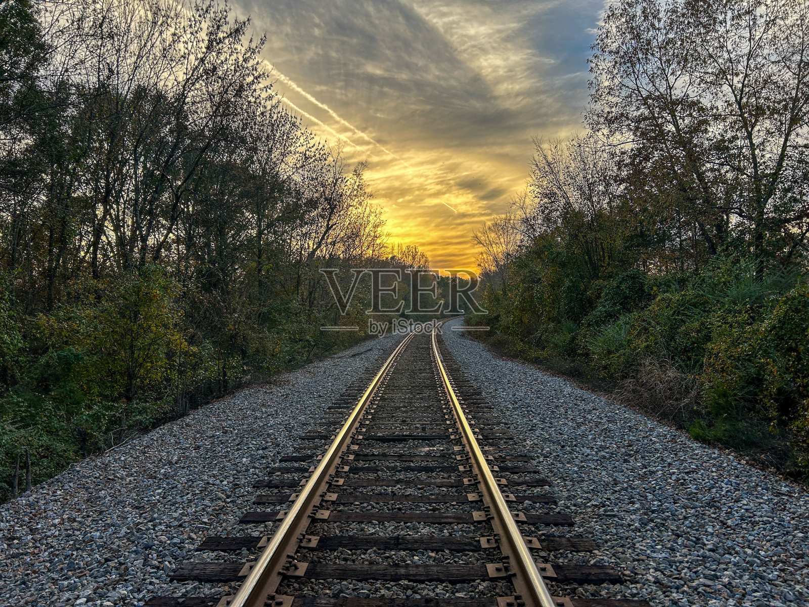 一条空无一人的铁路，夕阳正落在铁轨后面，还有一座小山照片摄影图片