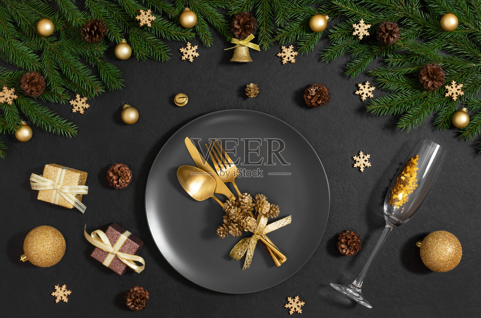 黑色的餐桌配上金色的圣诞装饰品和餐具。新年前夜的黑色背景。圣诞晚餐。俯视图，平铺。照片摄影图片
