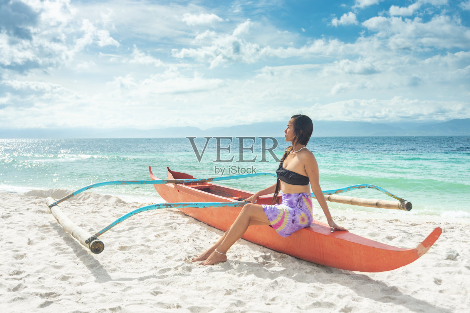 菲律宾宿务岛Moalboal的白色沙滩上，身着彩色泳装的迷人女子在船上摆姿势。照片摄影图片