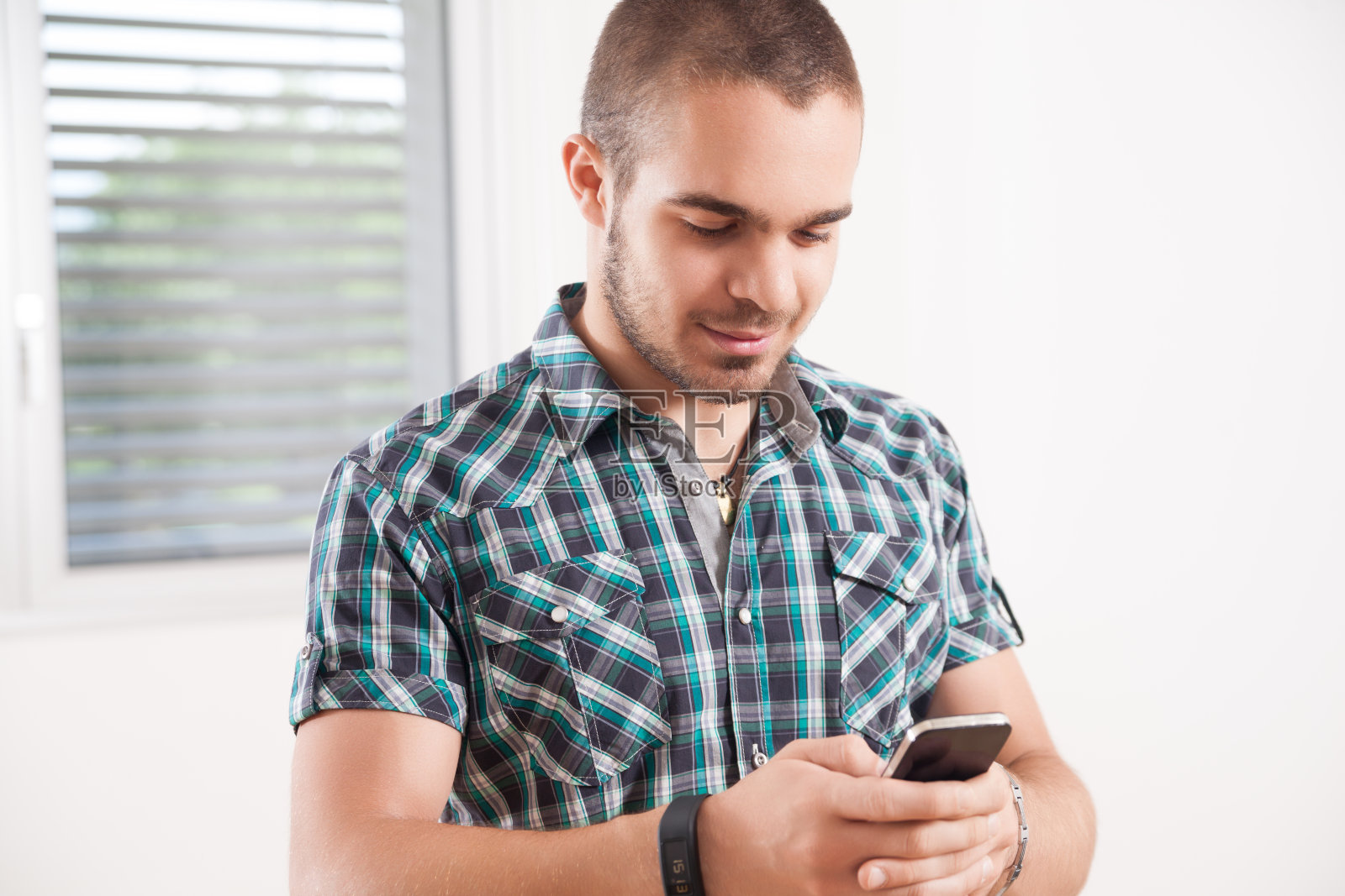 年轻的短发男子微笑着查看他的智能手机照片摄影图片
