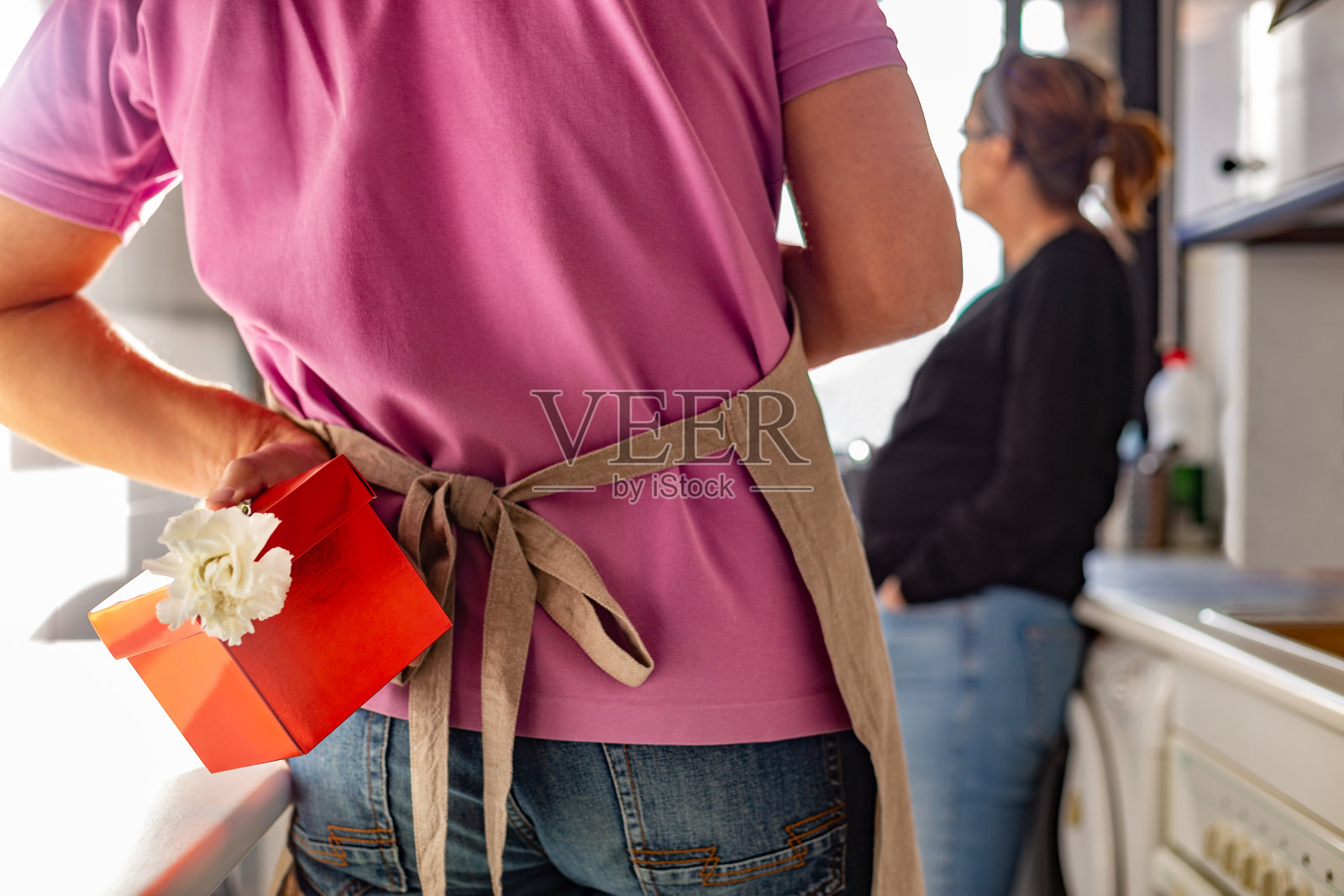 男人背对着窗边的女人，藏着礼物盒和鲜花照片摄影图片