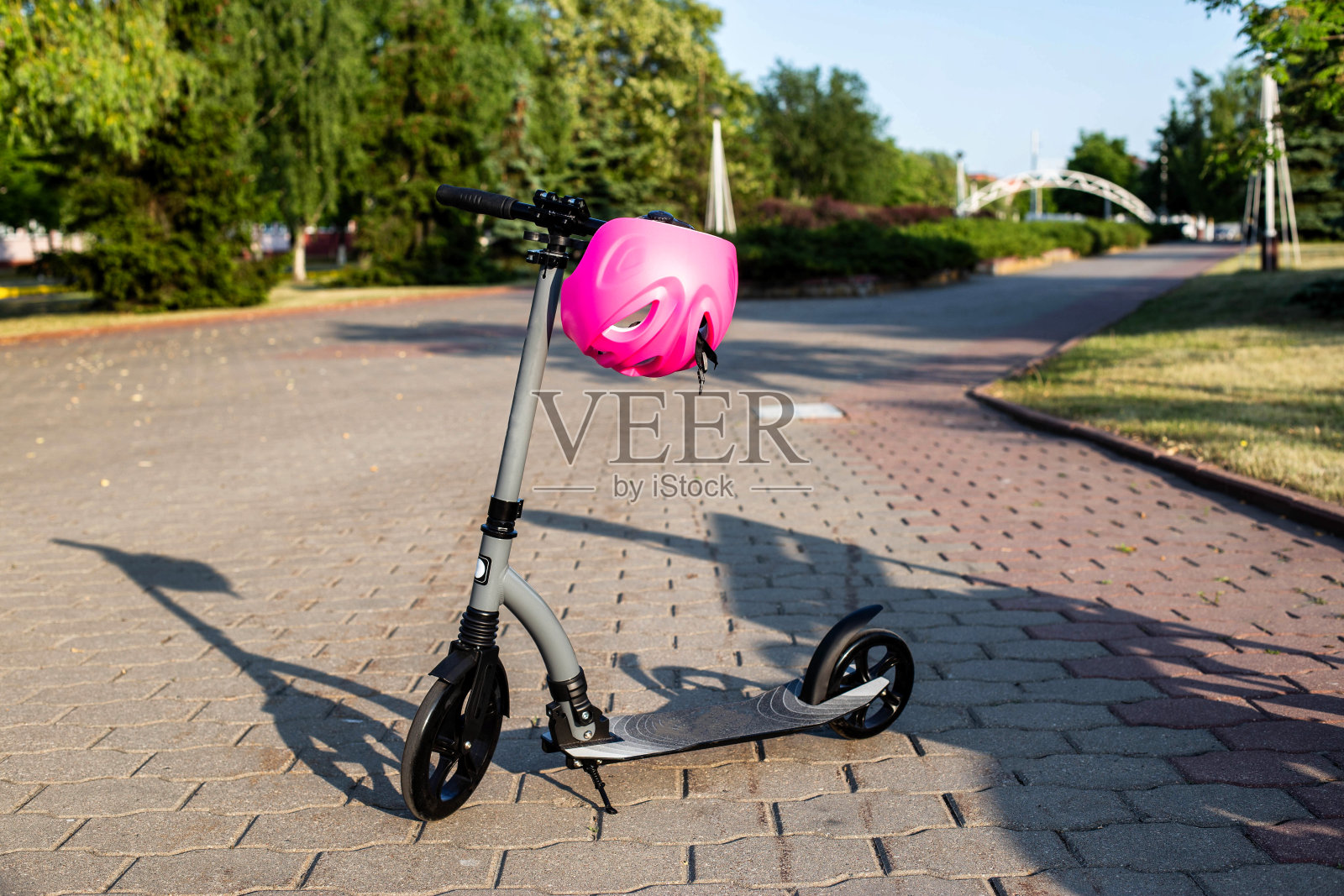 夏日夕阳的背景下，一辆戴着粉色头盔的现代摩托车停在一条小巷里。骑滑板车时的安全概念。文本复制空间照片摄影图片