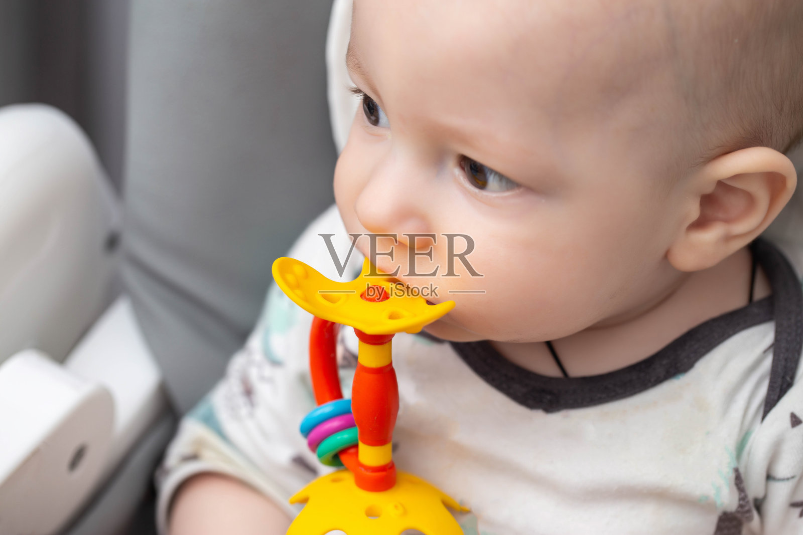 一个孩子的肖像，他咬了一个多色的玩具按摩器，用于儿童出牙。帮助孩子长牙。牙龈瘙痒和流涎，牙附件。照片摄影图片