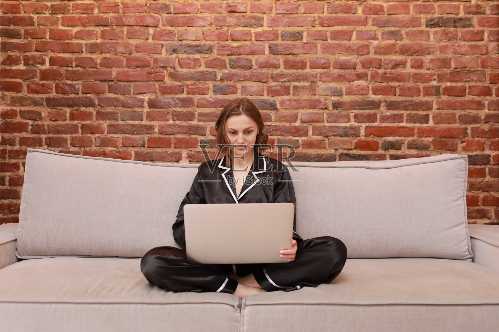 专注的年轻高加索女性盘腿坐在沙发上，使用笔记本电脑进行在线工作或在家学习。千禧一代女性在社交网络上阅读新闻，用即时通讯工具交流，网上购物照片摄影图片