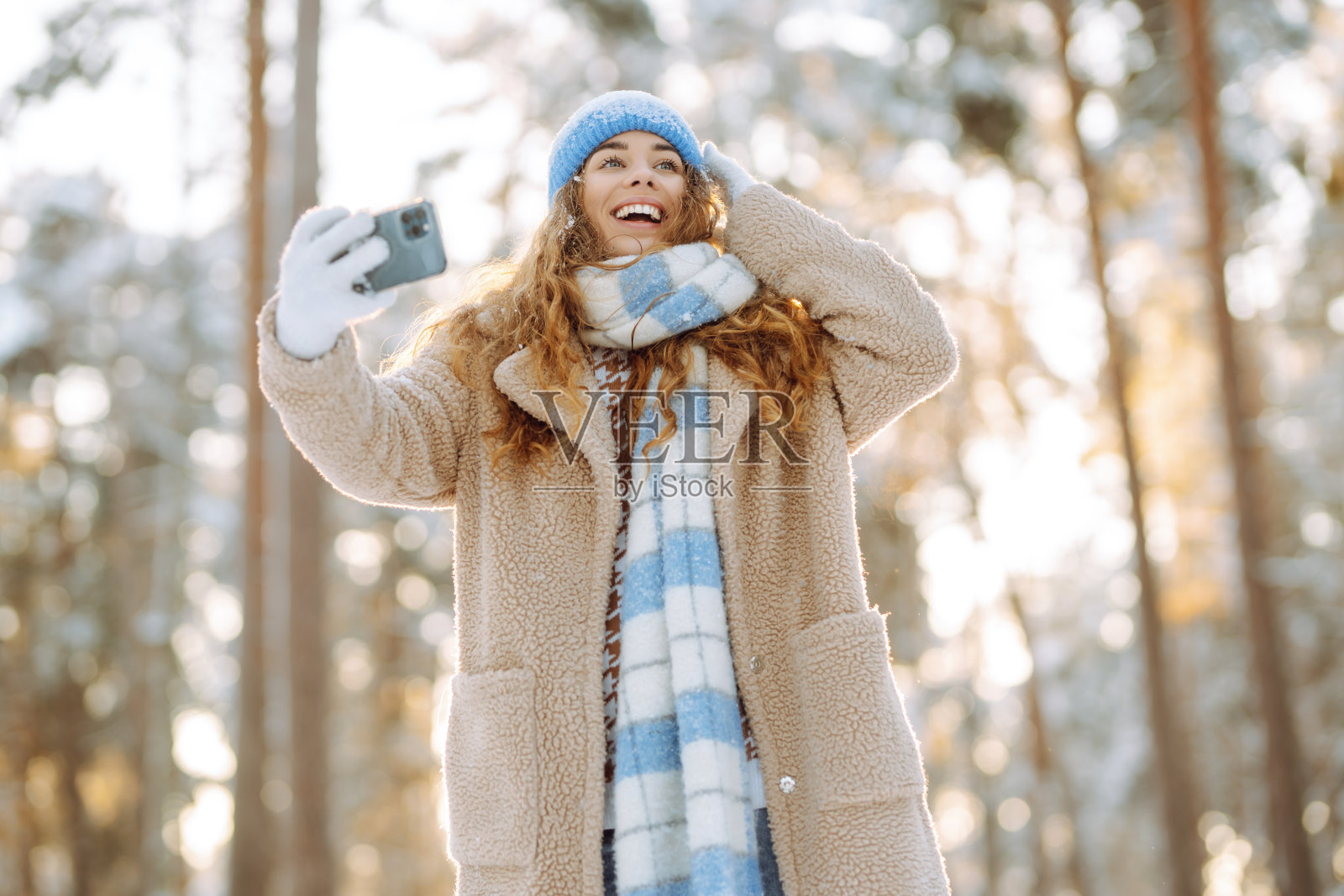 快乐的女人戴着鲜艳的帽子，围着围巾，手里拿着手机自拍。照片摄影图片