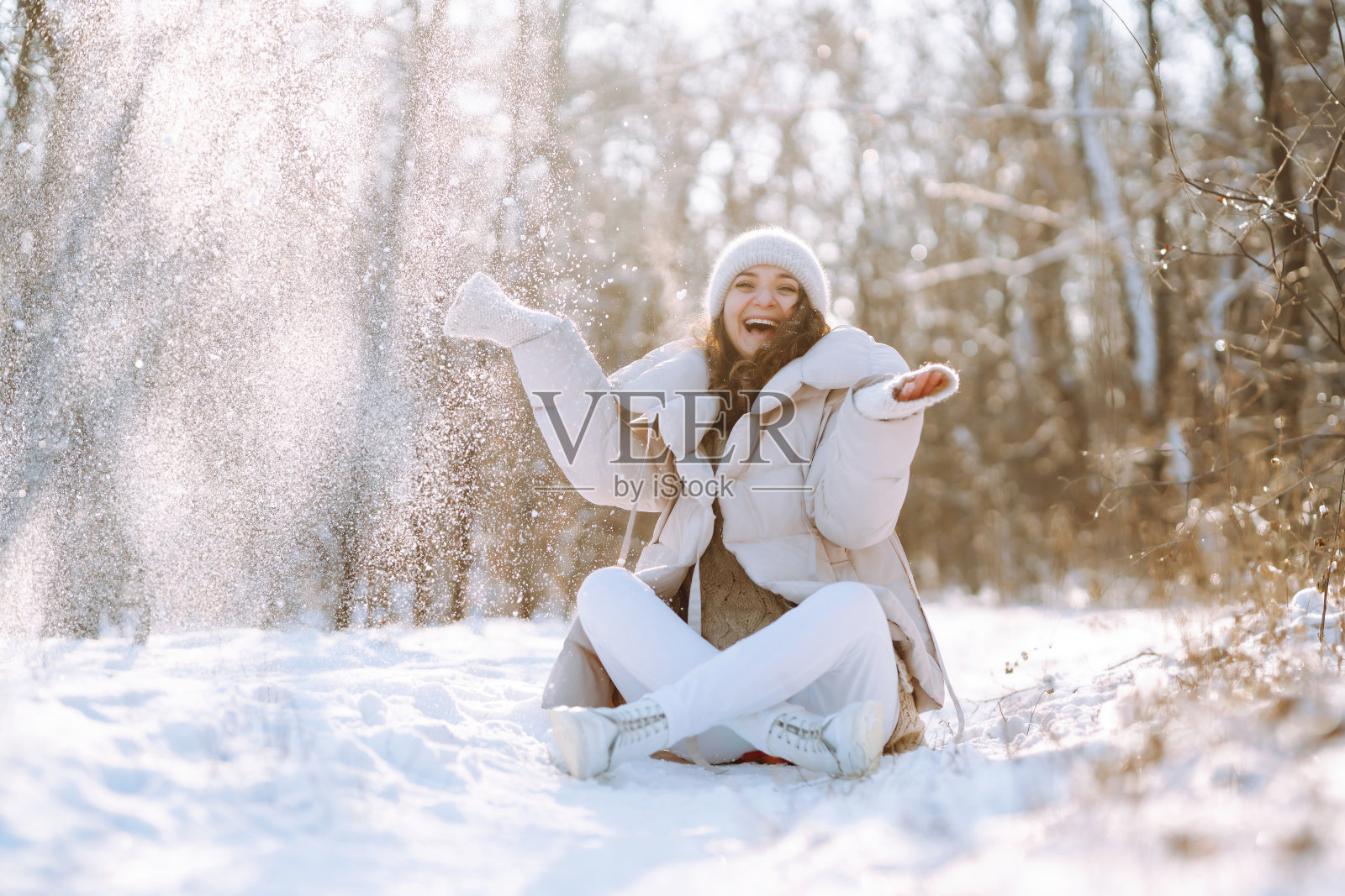 在一个阳光明媚、霜冻的日子里，一位穿着冬装、面带微笑的妇女走过一片白雪皑皑的森林。照片摄影图片