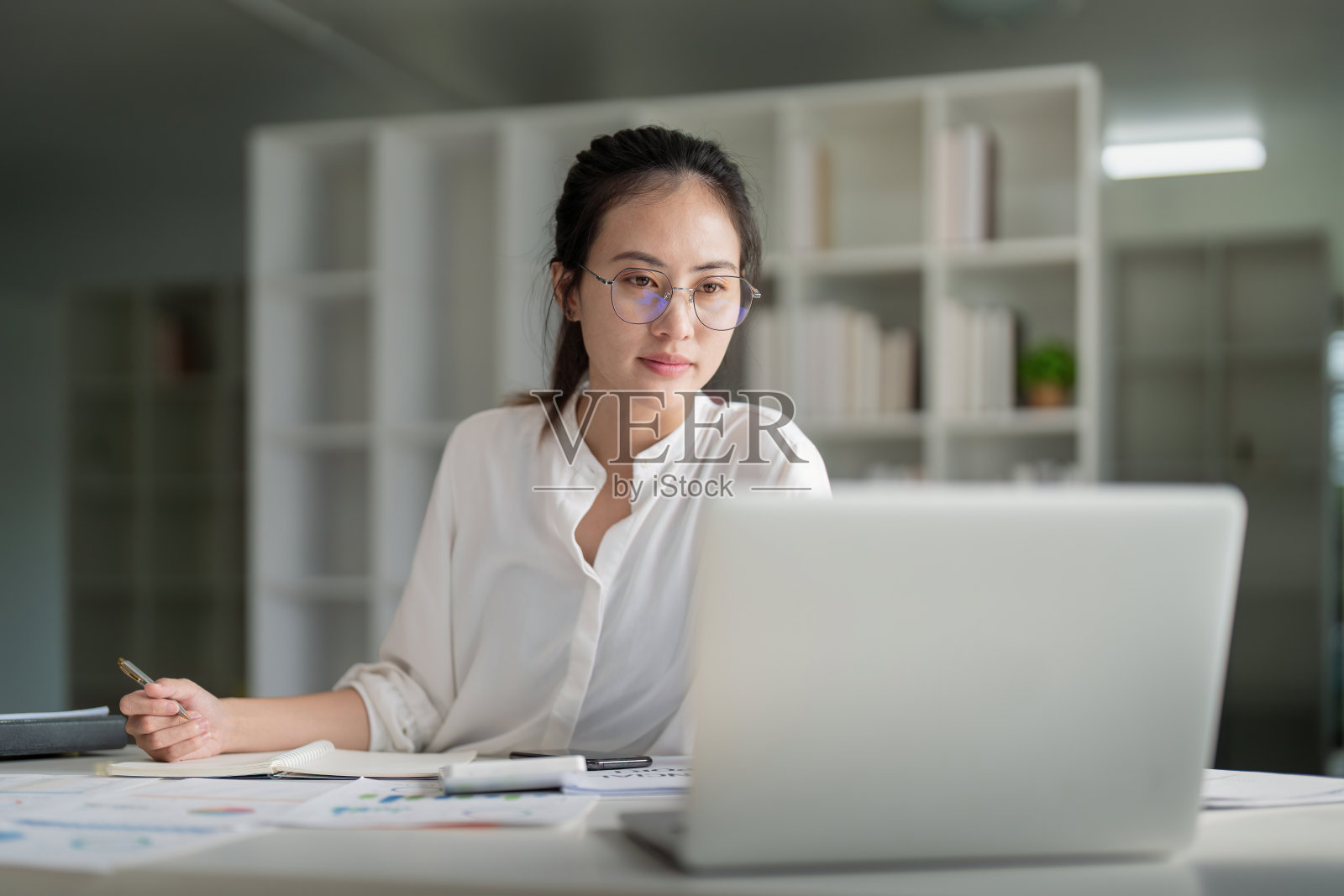 美丽年轻的亚洲女商人的肖像，坐在办公室现代化的工作站，在笔记本电脑上打字照片摄影图片