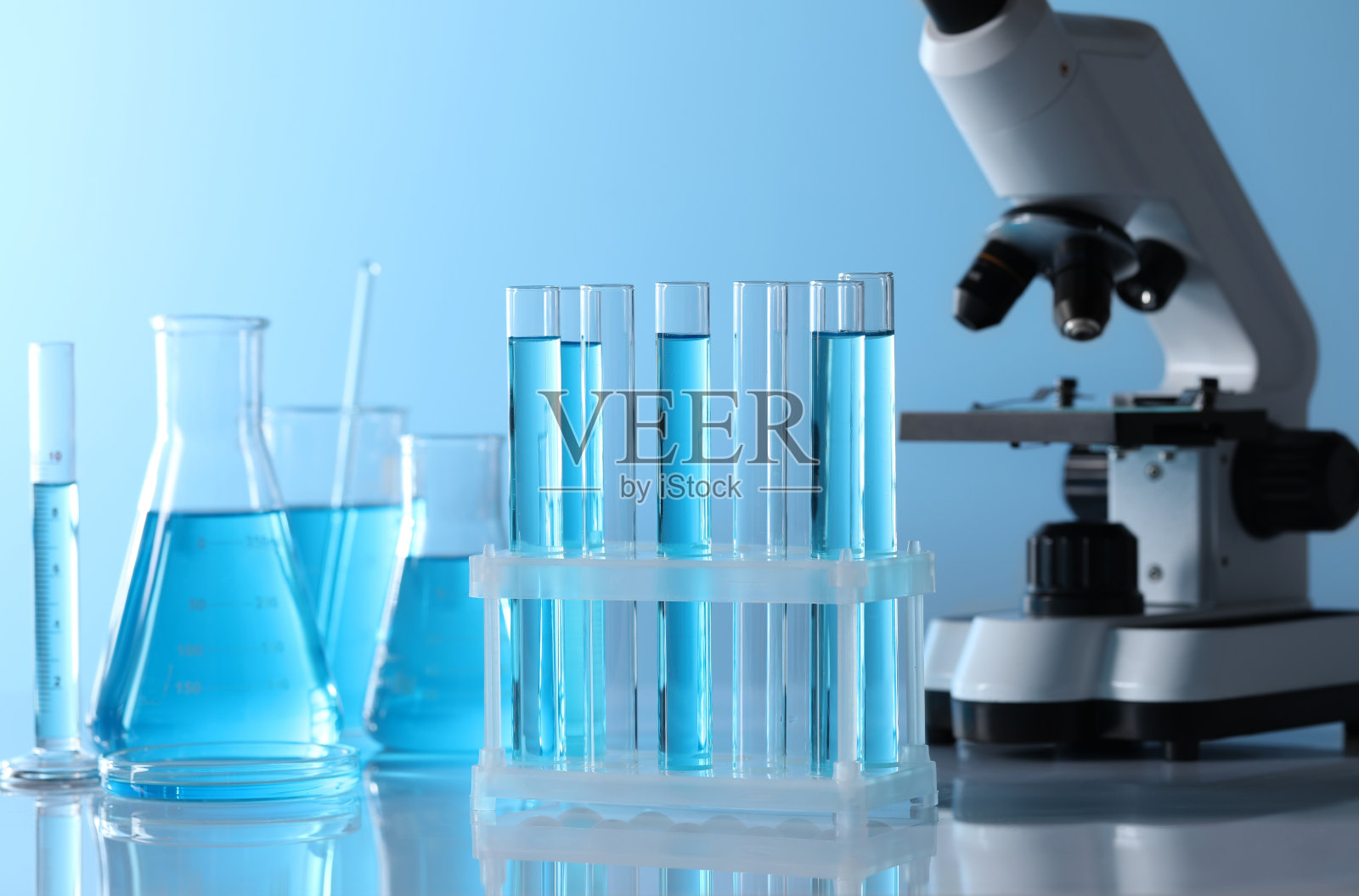 显微镜靠近不同的实验室玻璃器皿和试管，试管上有浅蓝色的液体照片摄影图片