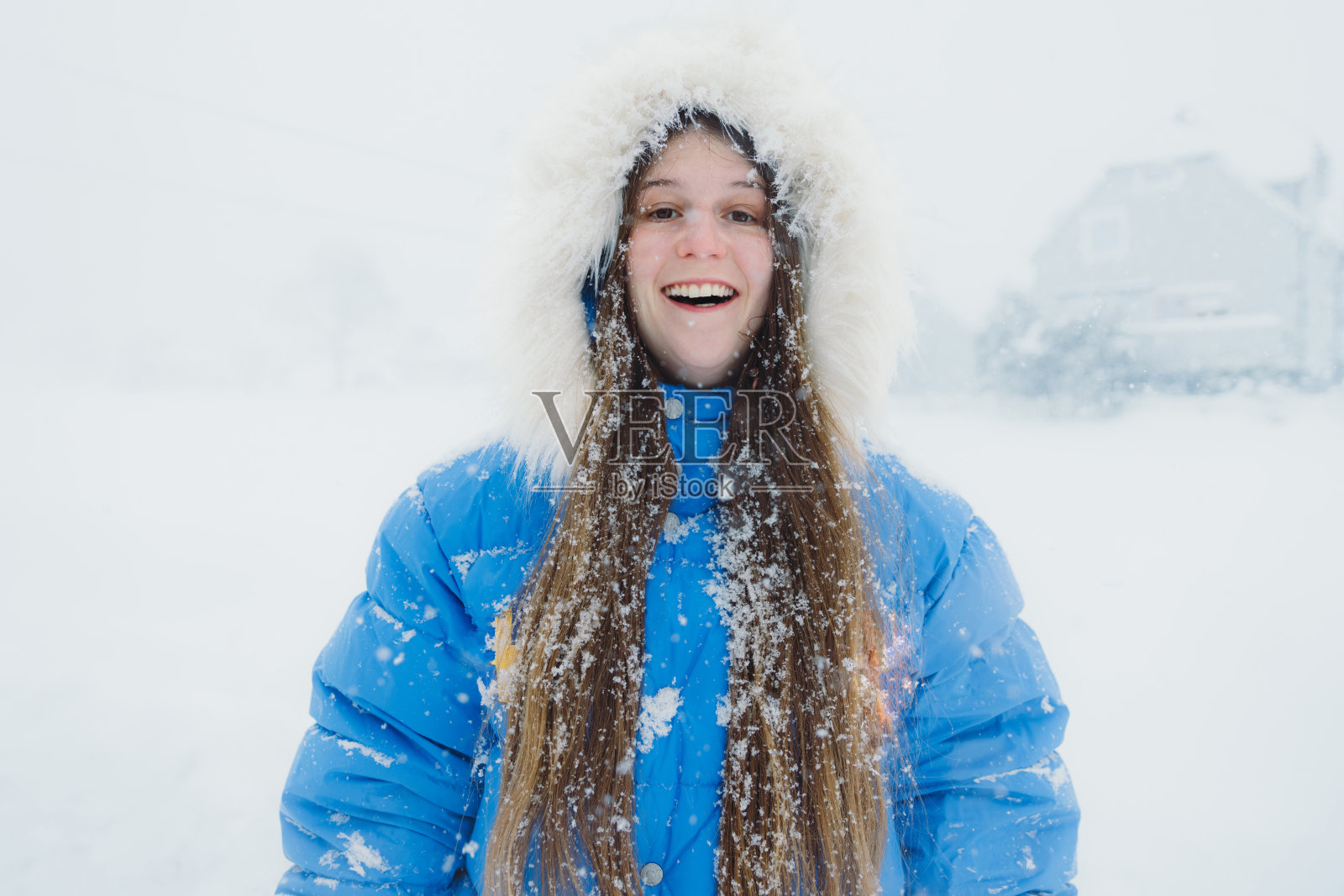 穿着蓝色外套的微笑女子欣赏冬日童话，在大雪中漫步在斯堪的纳维亚村庄照片摄影图片