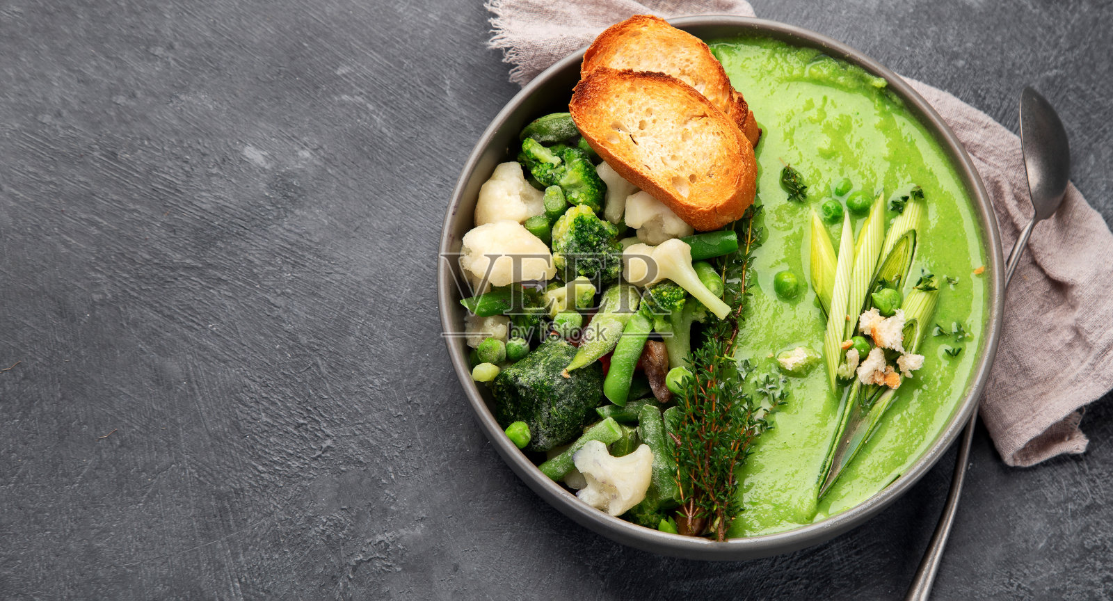 美味健康的绿色奶油汤放在碗里，桌上放着面包丁。照片摄影图片