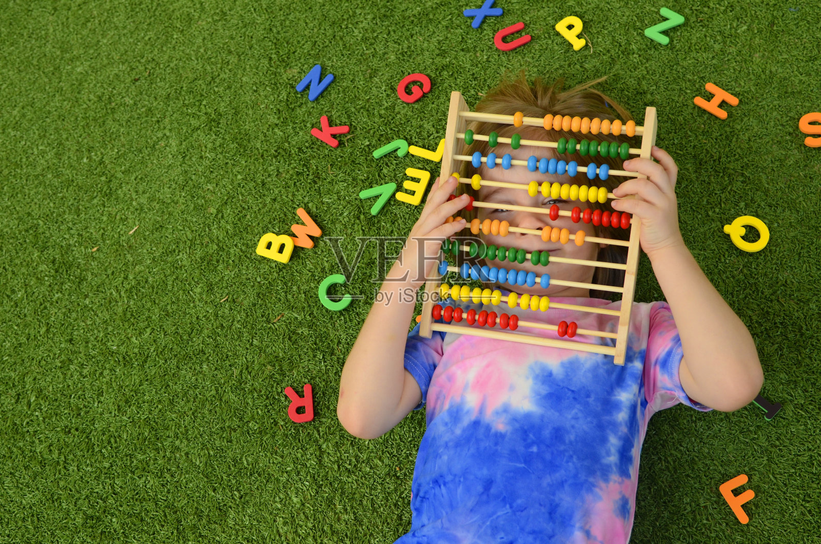 孩子学习字母和数字，男孩藏在木制算盘后面，看不到脸，彩色英文字母照片摄影图片