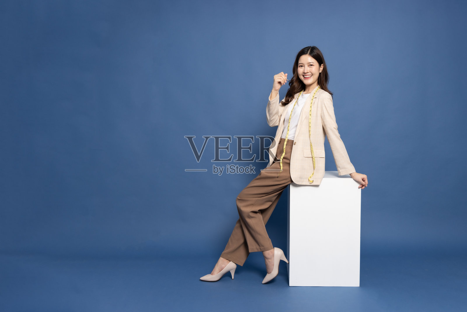 年轻的亚洲女商人坐在蓝色背景的白色盒子上，全身构图照片摄影图片