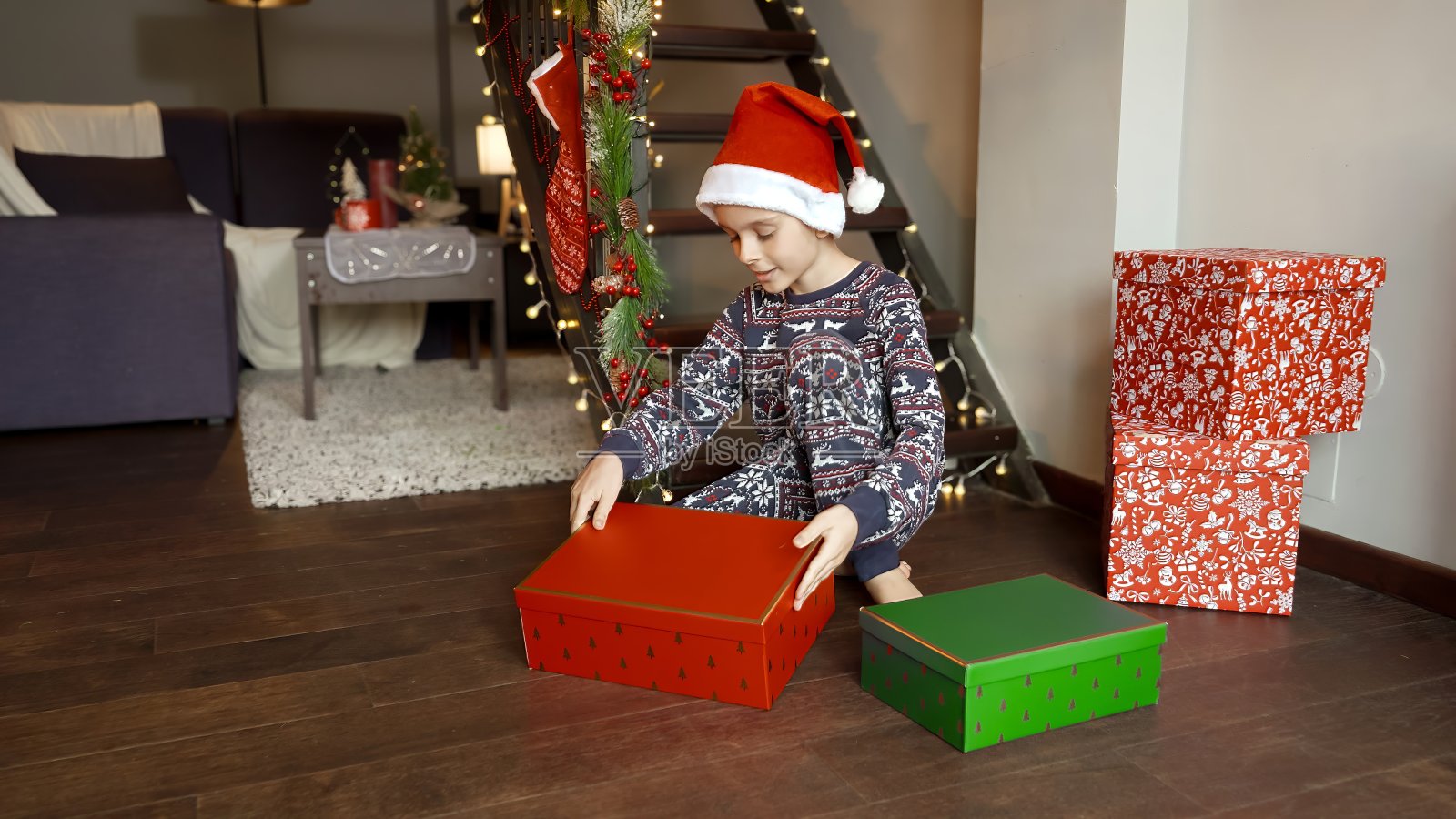 穿着睡衣的小男孩早上坐在地板上打开圣诞老人送的圣诞礼物照片摄影图片