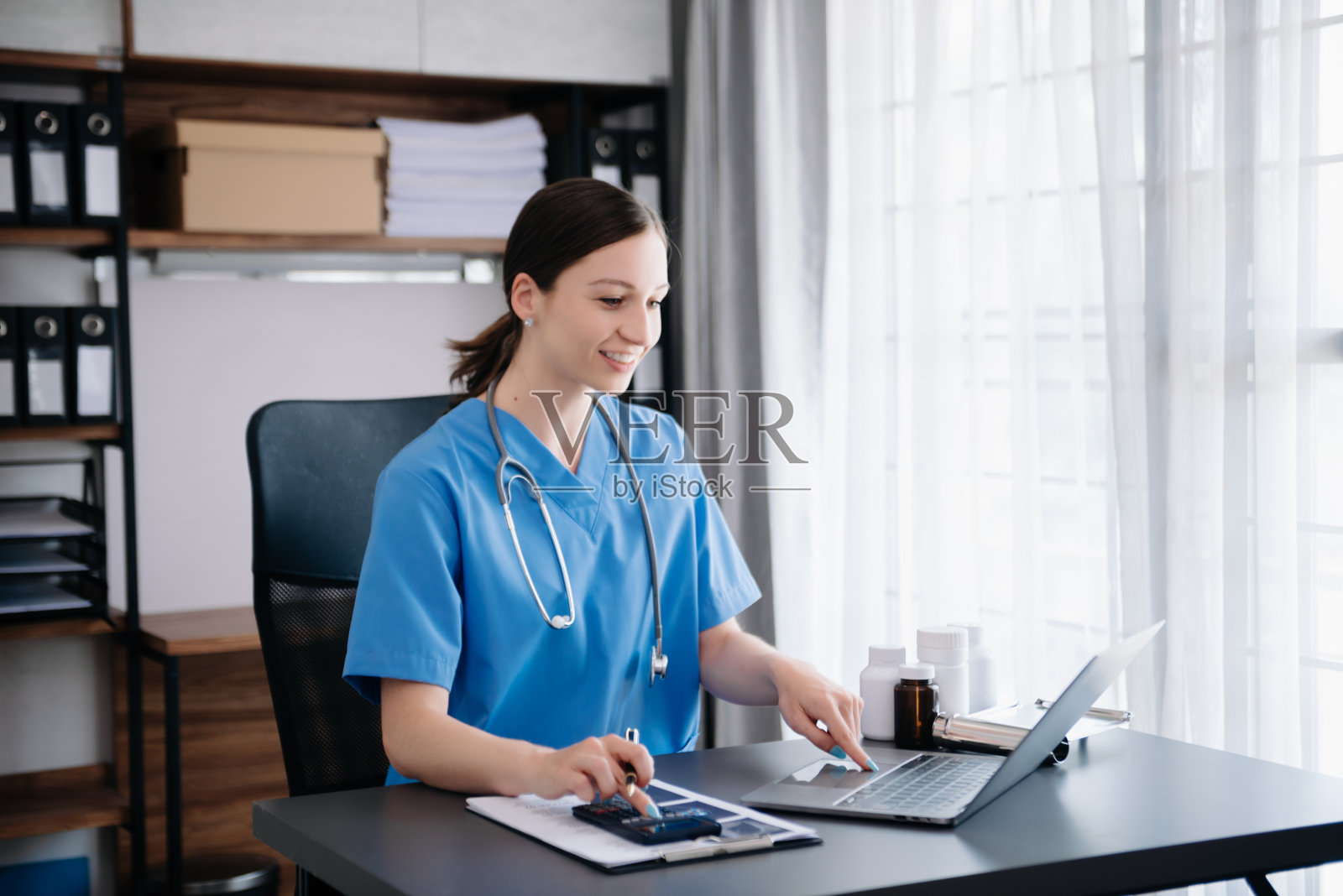 医疗技术理念。女医生在现代办公室用手机和听诊器工作照片摄影图片