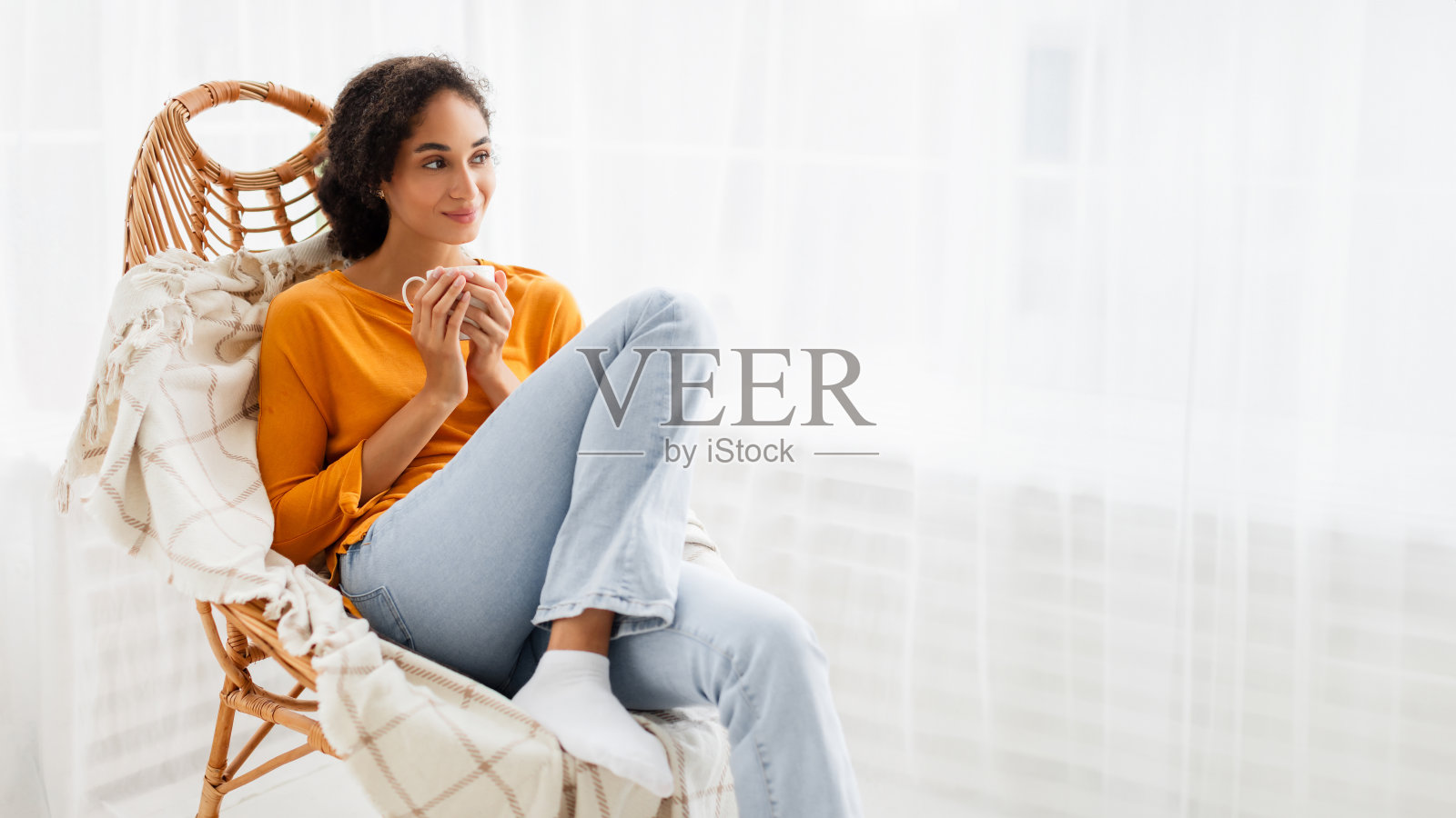 放松的年轻女士拿着咖啡杯坐在室内的扶手椅上照片摄影图片