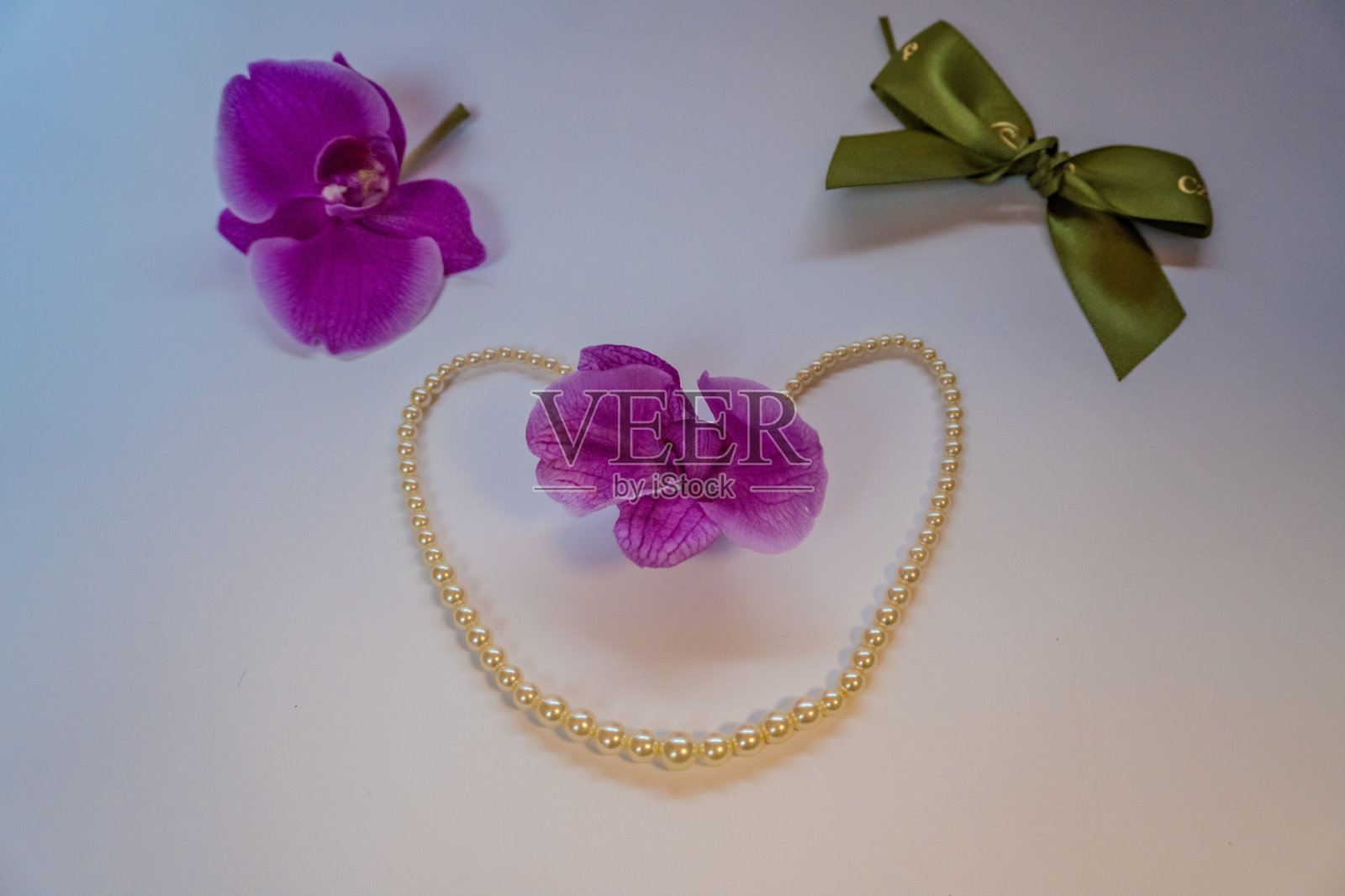 一条白色珍珠项链呈心形，上面有一朵紫色的兰花照片摄影图片