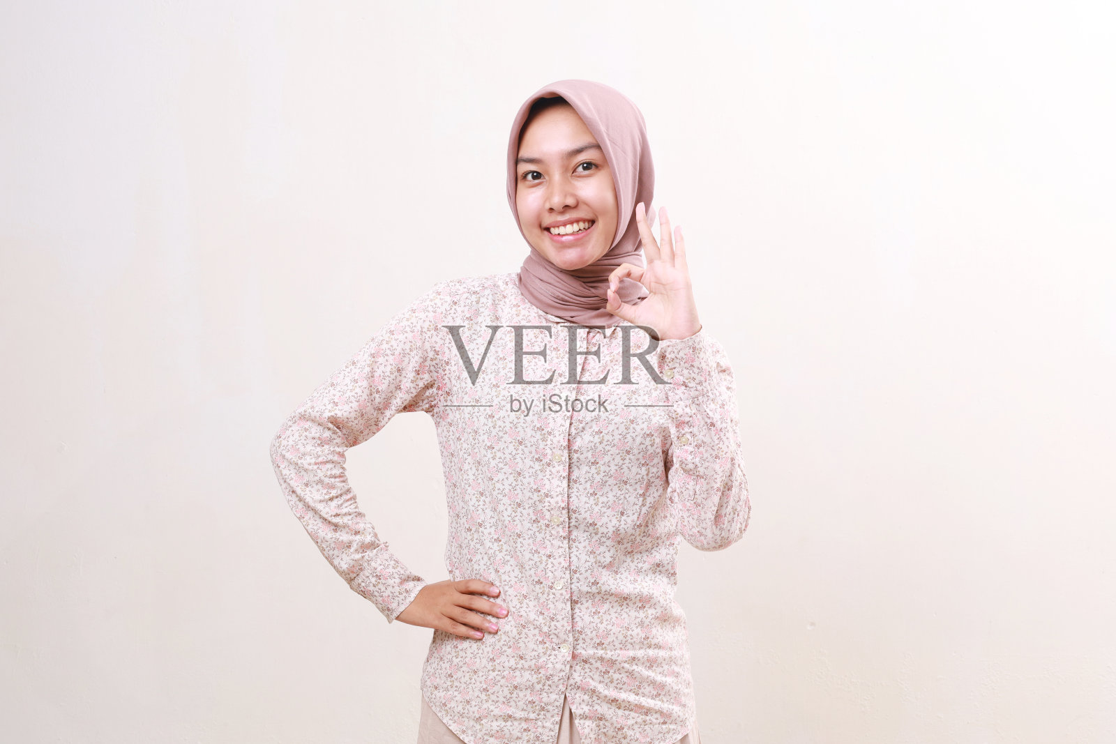 满意的年轻亚洲穆斯林妇女站着，同时做出合适的手势。隔离在白色背景上照片摄影图片