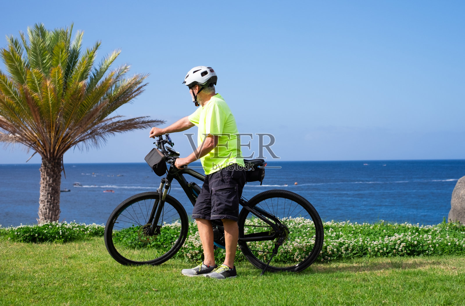 老年运动男子骑着电动自行车在海上户外远足。戴头盔的老人享受着自由和健康的生活方式照片摄影图片
