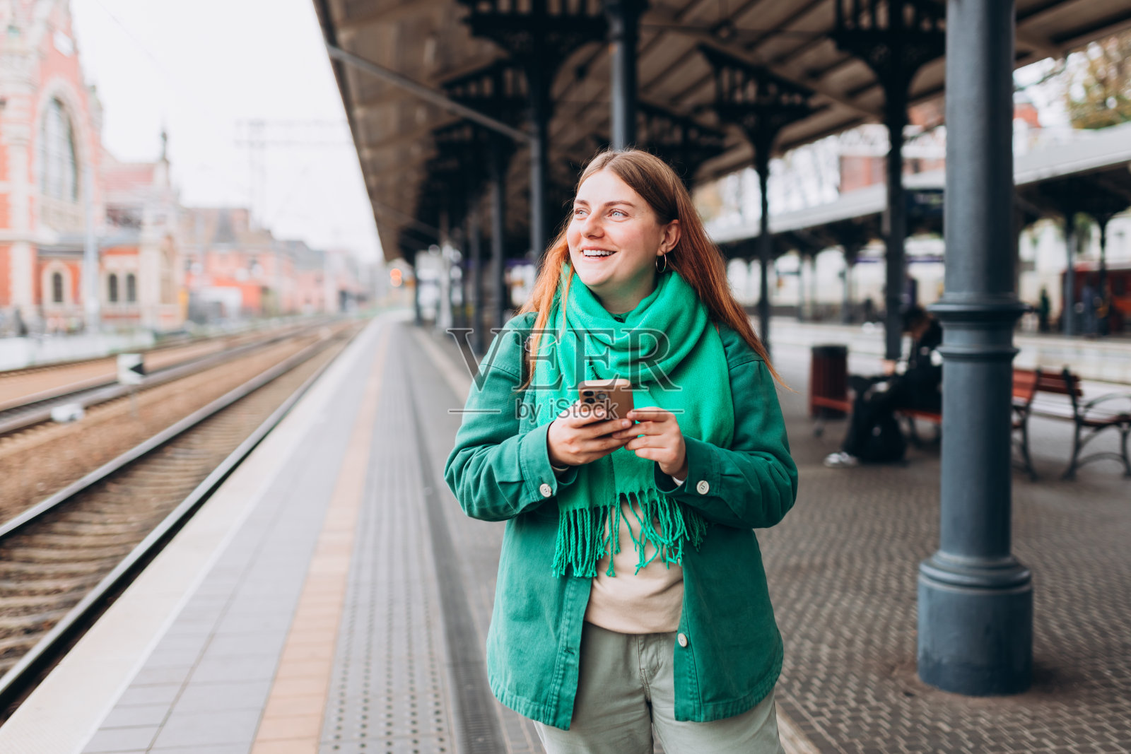 一个年轻漂亮的女人背着双肩包，一边用手机一边等火车。乘客使用手机通过应用程序监控交通时刻表照片摄影图片