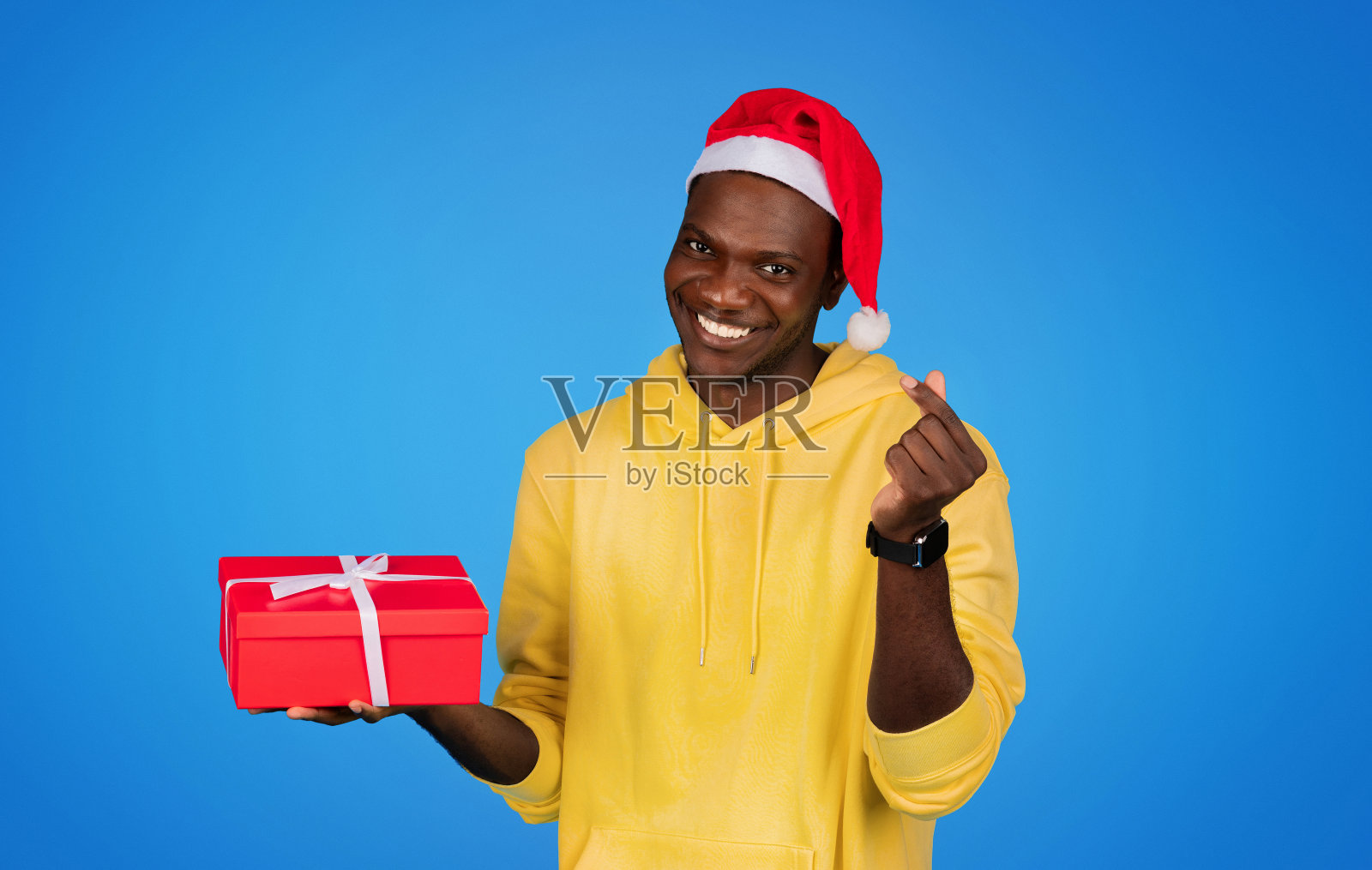 快乐的千禧一代非洲裔美国人，戴着圣诞帽，手里拿着礼盒，做着手势照片摄影图片