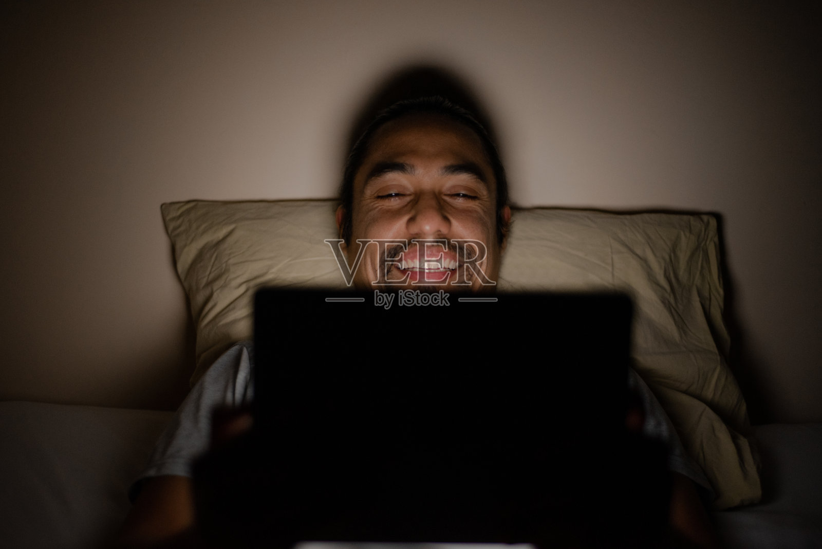 一个男人开心地微笑着在他的平板电脑上看电影。照片摄影图片