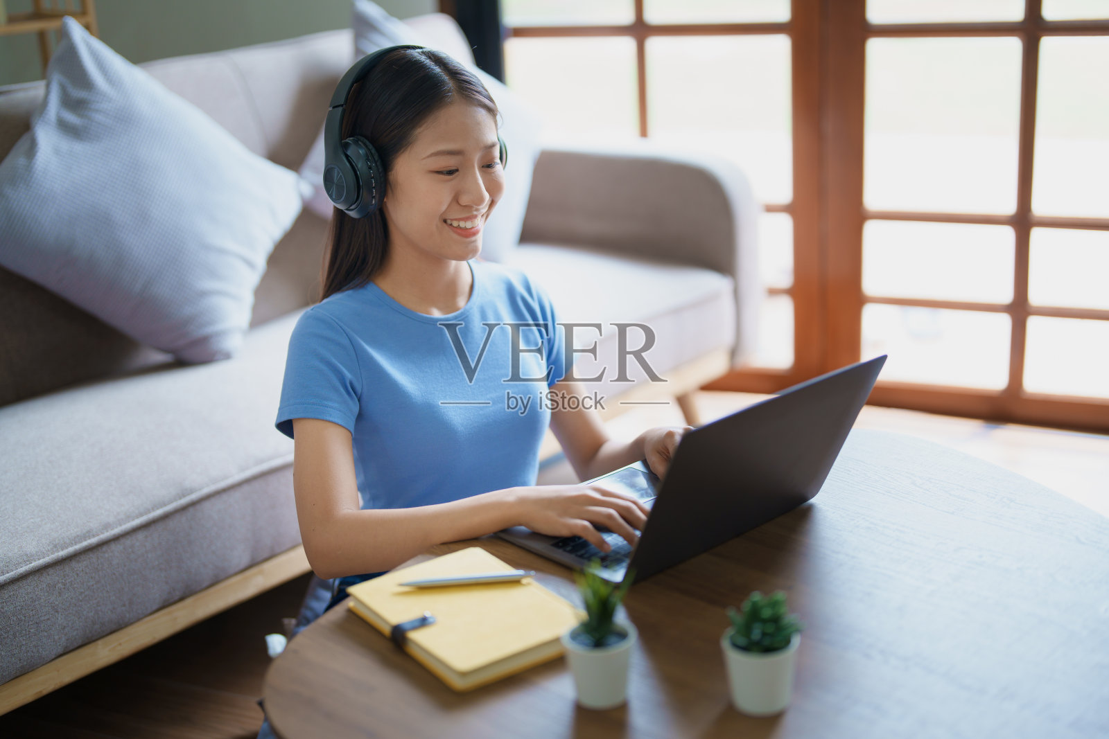 女人戴着耳机坐在舒适的沙发上，用电脑和笔记本电脑听音乐。照片摄影图片