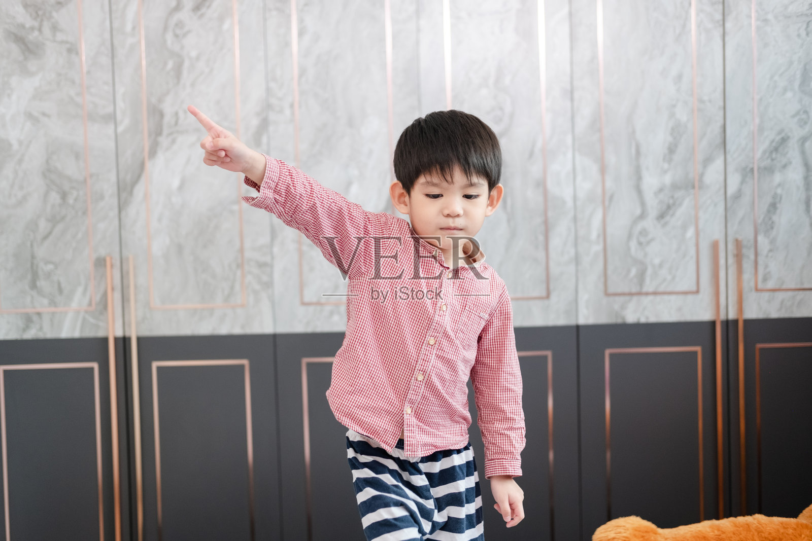 一个亚洲男孩站着，双手指向一边。照片摄影图片