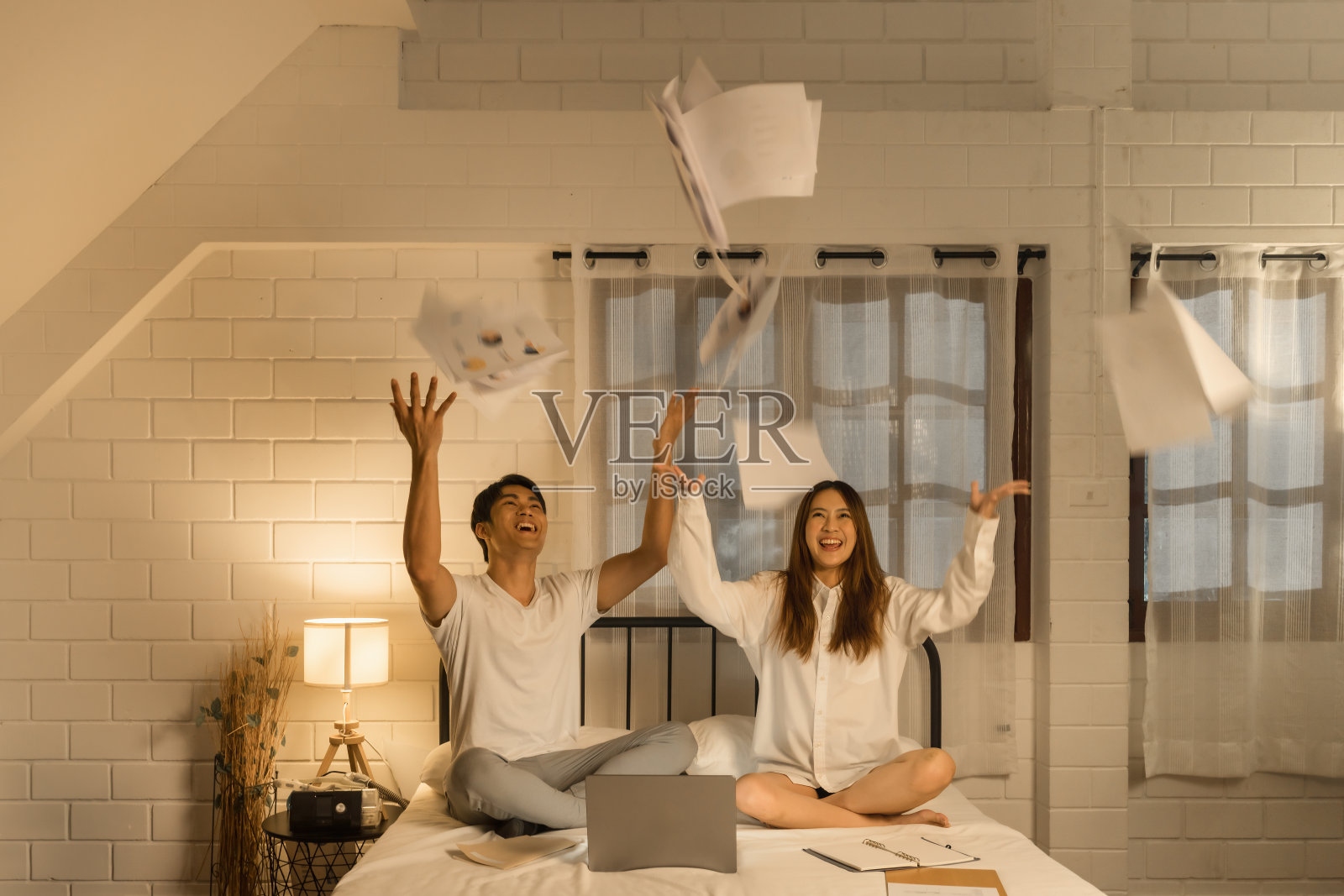 快乐的亚洲夫妇用财务图表和商业报告庆祝成功，报纸在家庭办公室里飞来飞去照片摄影图片