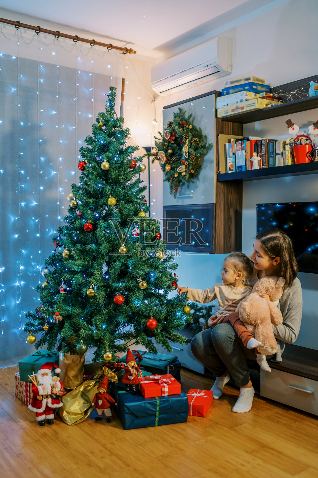 小女孩坐在妈妈的腿上给妈妈看圣诞树上的球照片摄影图片