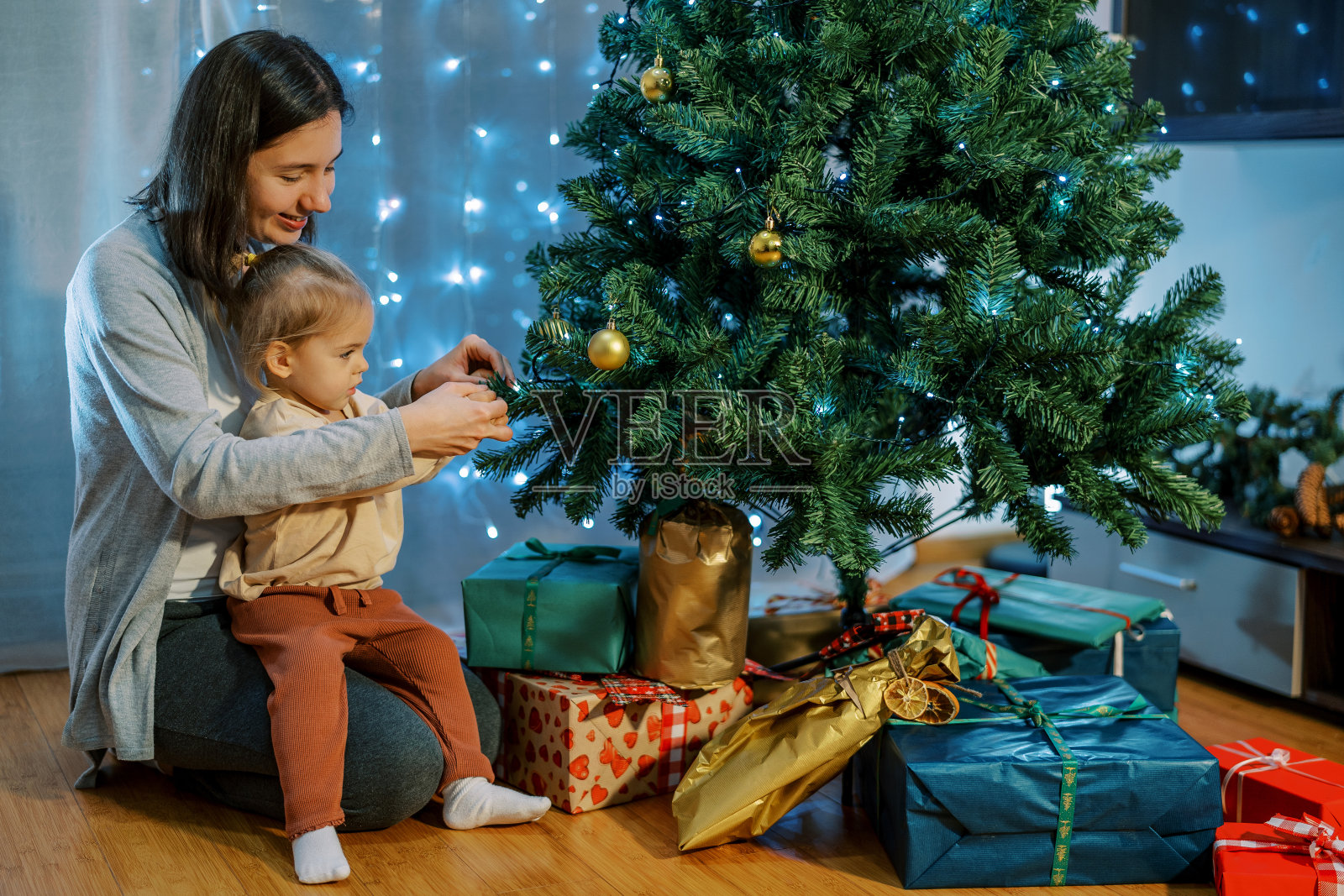 妈妈带着一个跪着的小女孩坐在地板上，把球挂在圣诞树上照片摄影图片