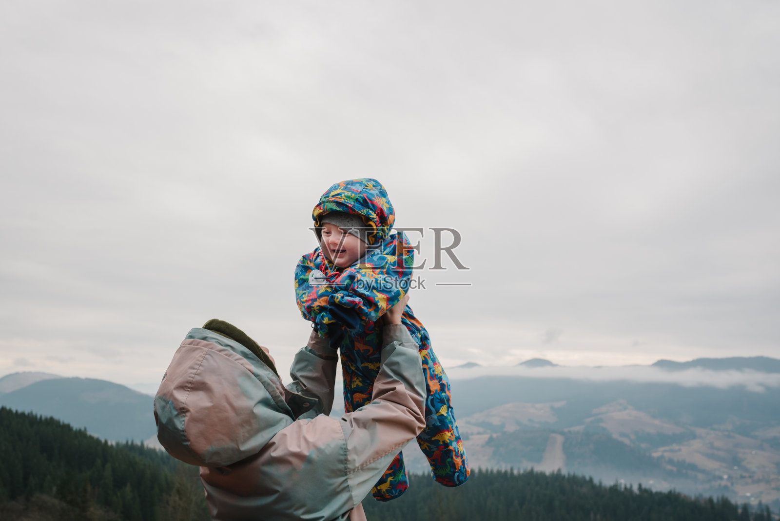 秋天的一天，母亲把儿子抛向天空。带着孩子去山里度假。人们在乡村站着放松。妈妈拥抱孩子享受在一起的时光。积极的周末旅游理念照片摄影图片