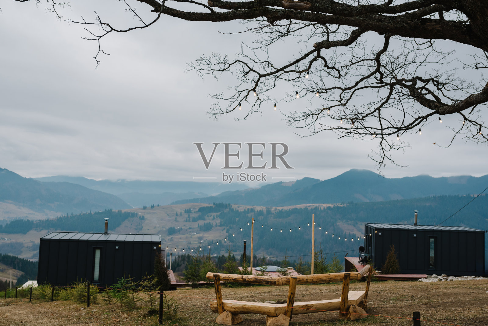 一个在黑房子后院有篝火的地方。带日落山景的小屋露台。绿草如茵的小山上的一所小房子，非常适合独自度假。春天或秋天的现代建筑。照片摄影图片