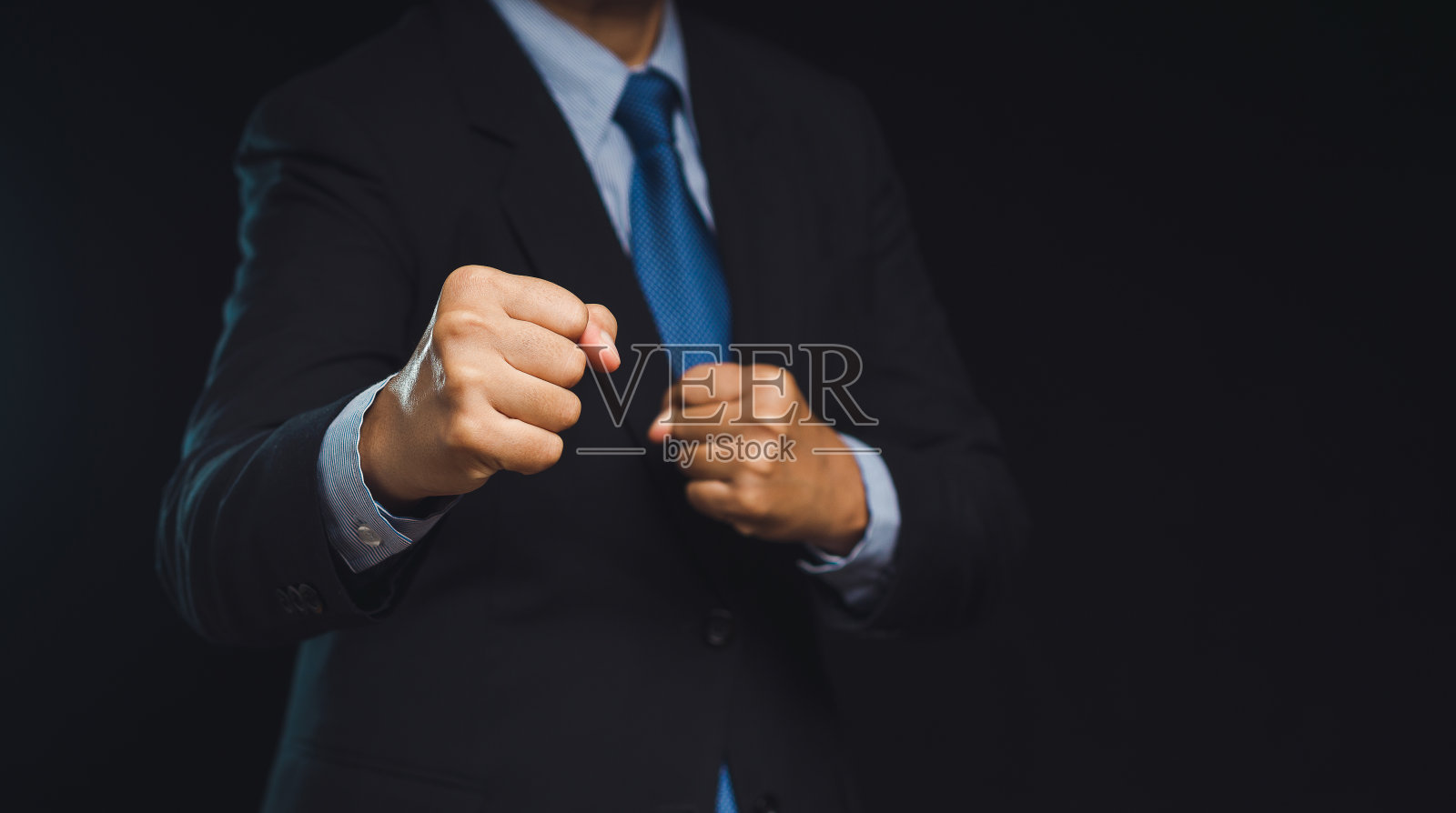西装革履的商人站在黑色背景上，举起拳头照片摄影图片