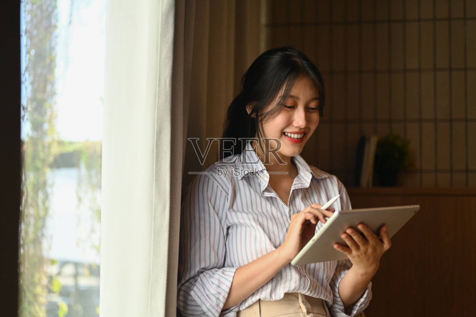 微笑的创意女性站在办公室窗口摆弄着数码平板电脑照片摄影图片