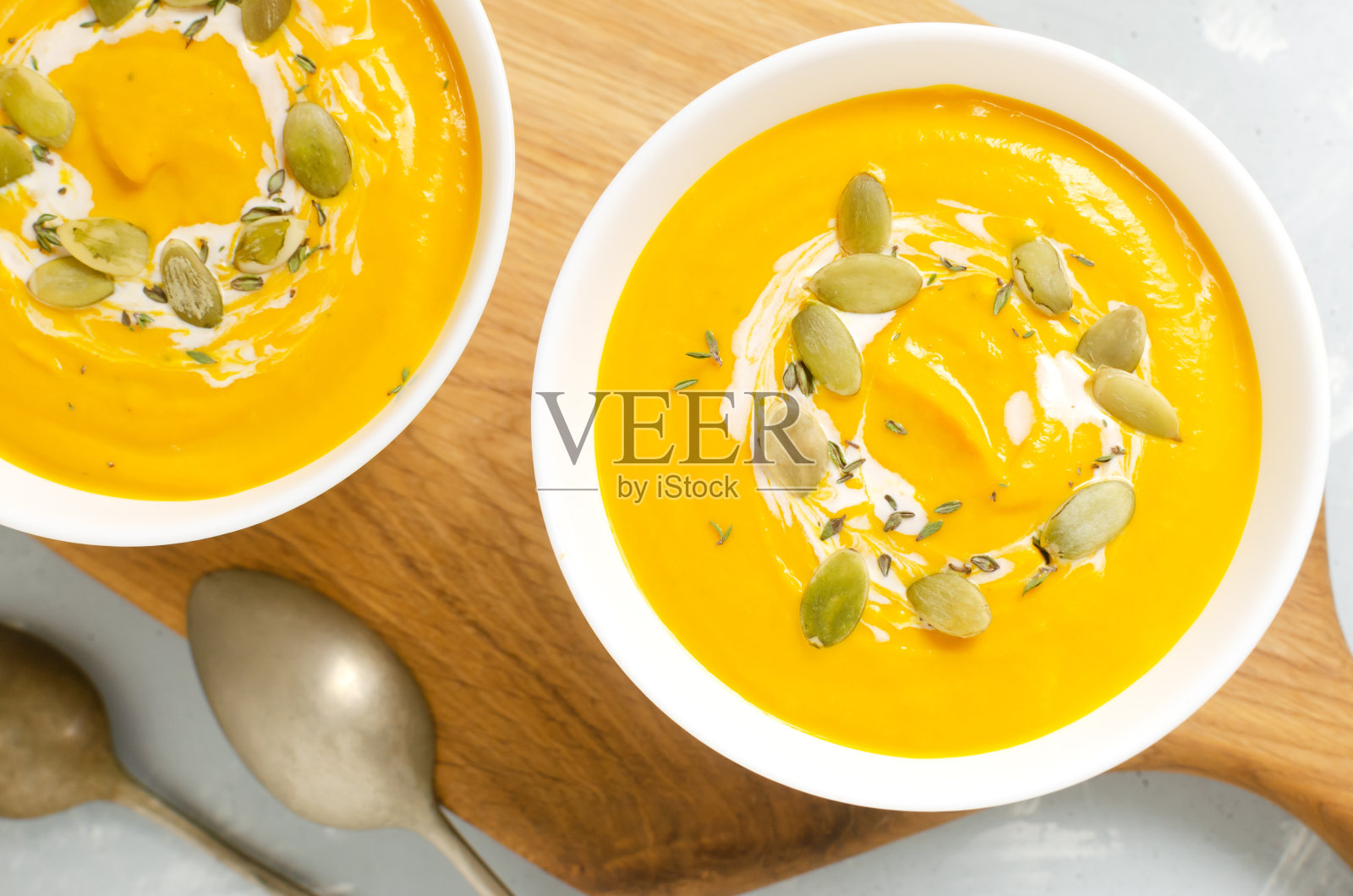 两碗白色的南瓜奶油汤，干种子和百里香叶放在灰色背景的木制砧板上。健康饮食的概念。素食和纯素食品。俯视图照片摄影图片