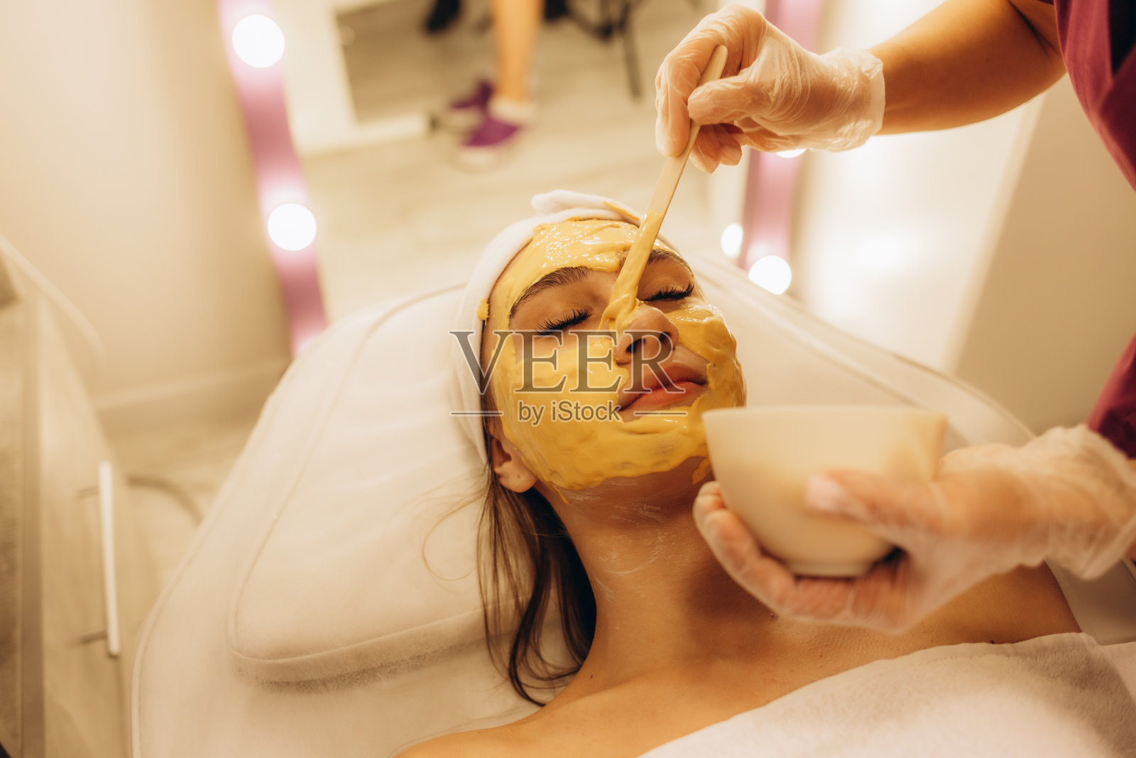 美容师给一位女士敷上黄色海藻酸盐面膜照片摄影图片