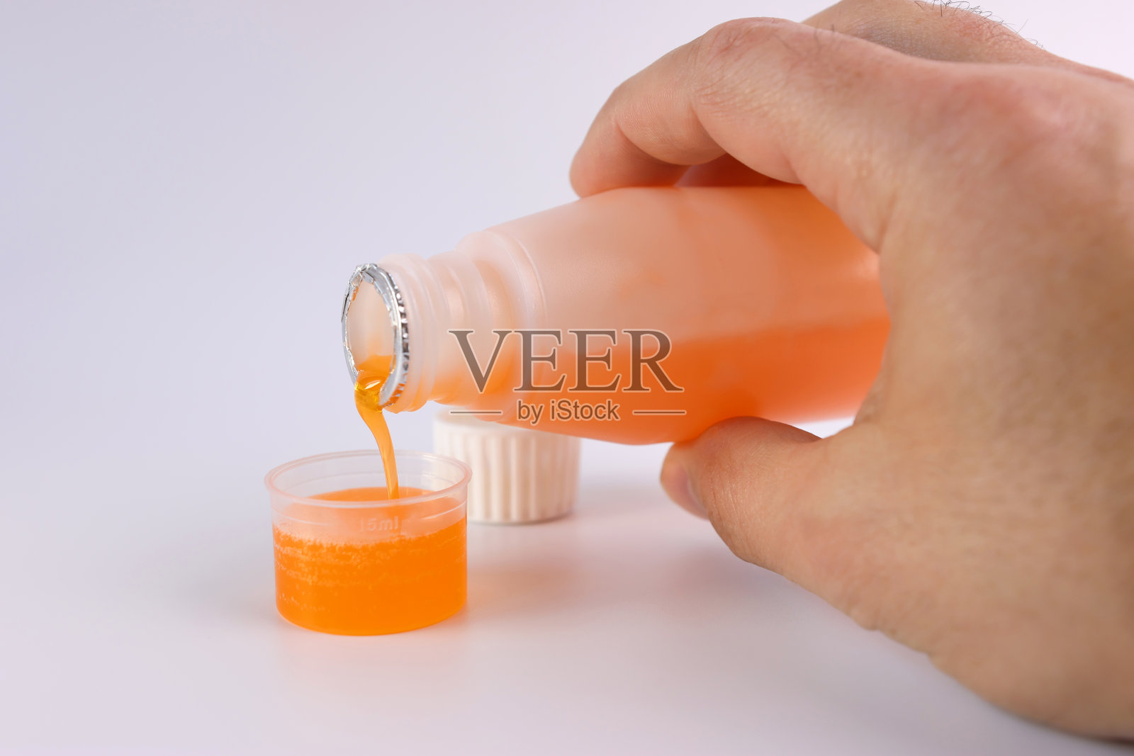 药用糖浆倒入一个白色背景上有液体体积划分的容器中。治疗和预防疾病。加强免疫力。照片摄影图片