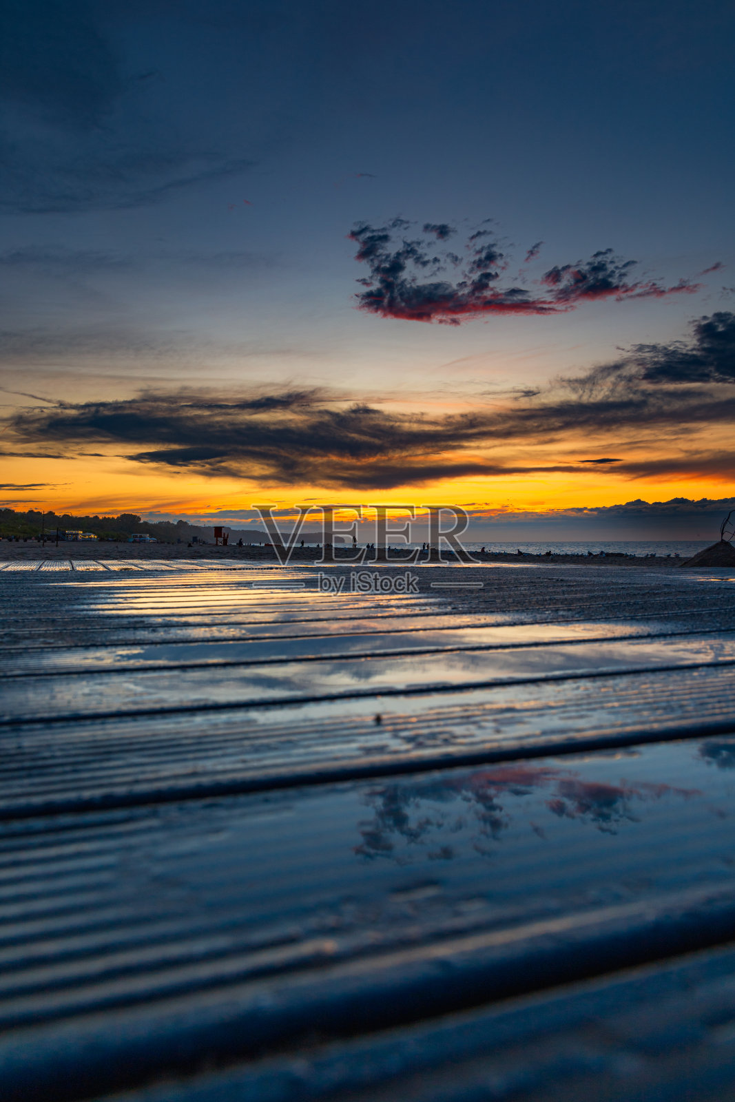 美丽的金色日落在黄金时间在海滩旁边的黑暗和寒冷的大海，在夏天的风暴和雨水反射在水坑上的木制平台面板照片摄影图片