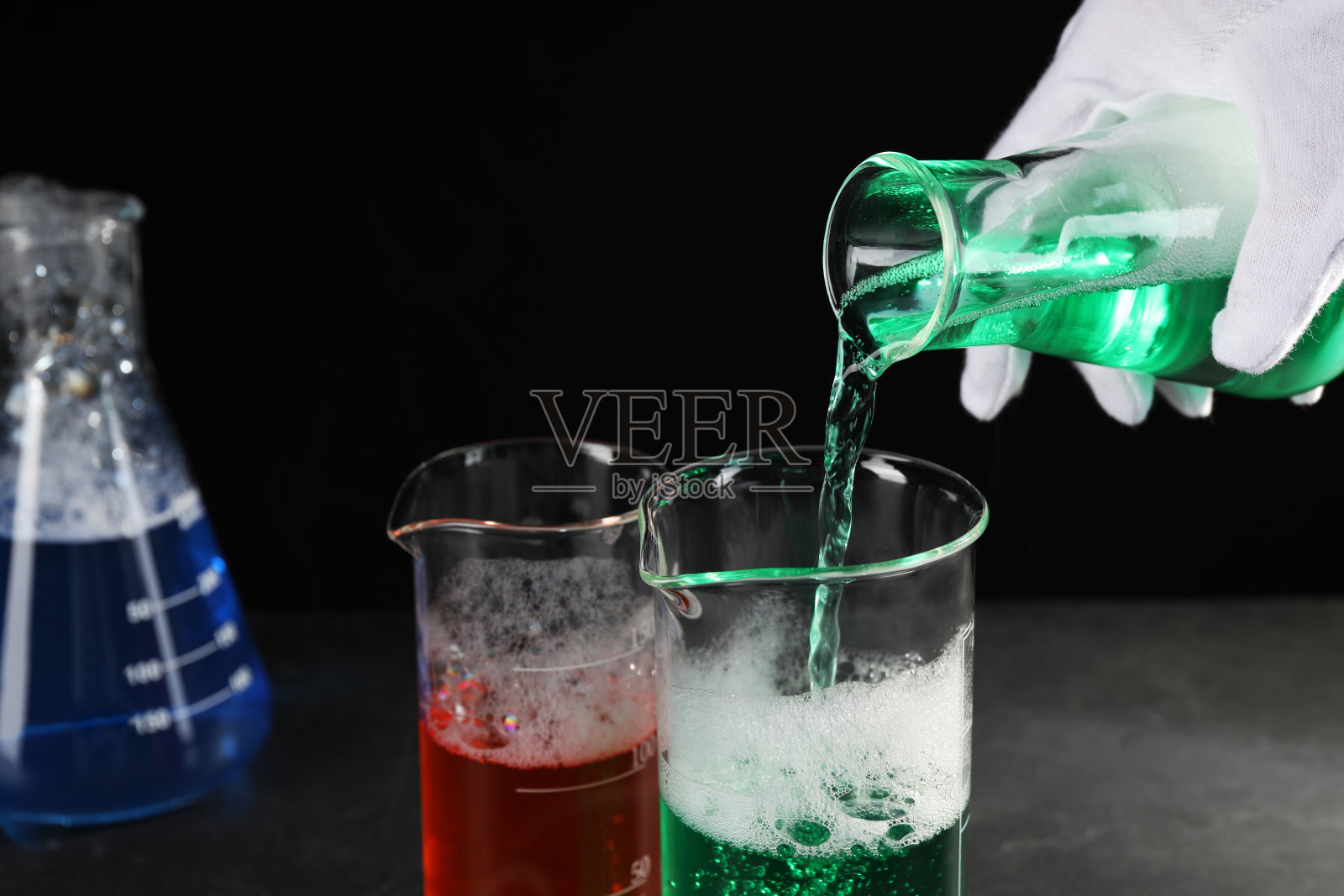 科学家在黑色的桌子上摆弄实验室的玻璃器皿(特写)。化学反应照片摄影图片