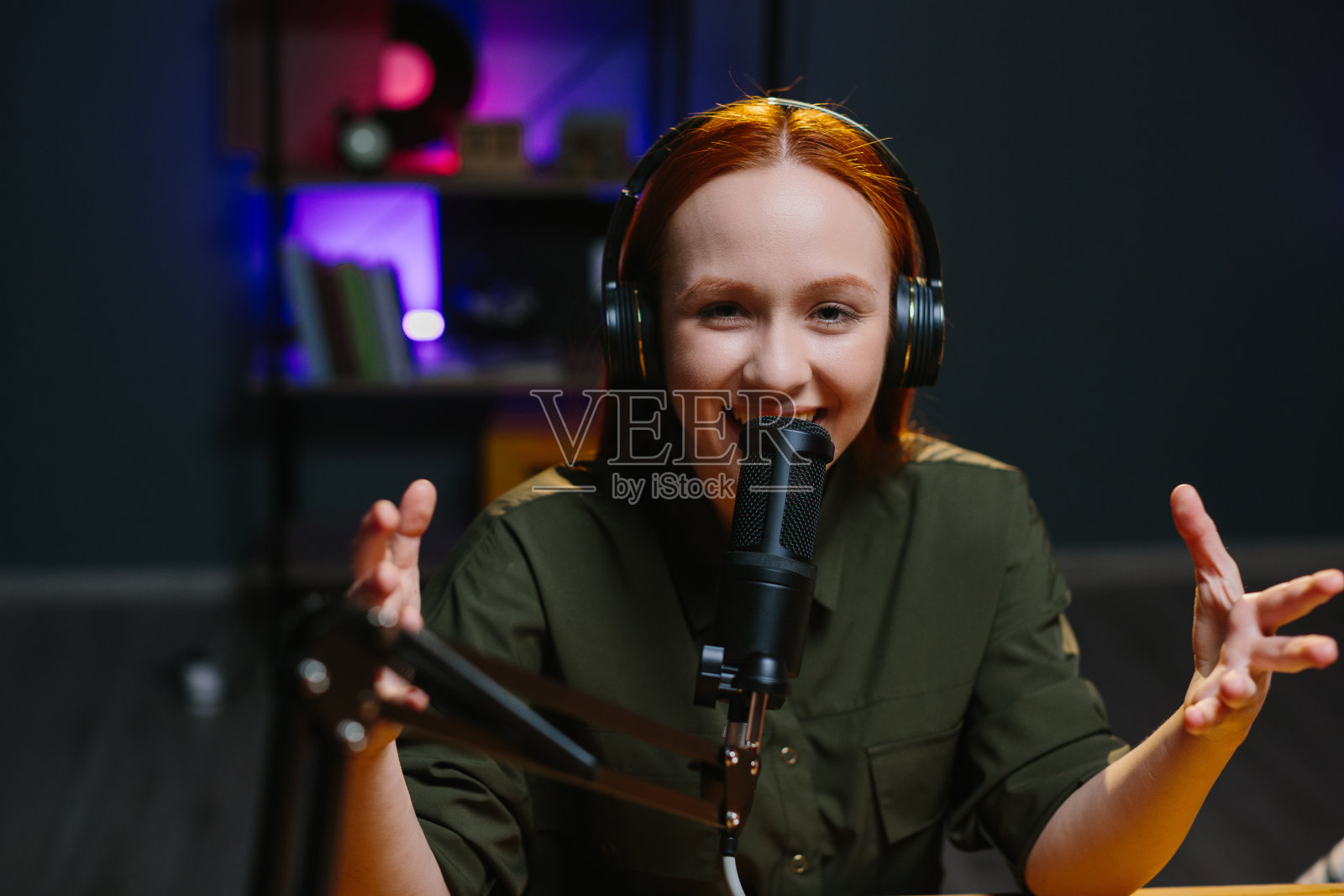 一个戴着耳机的女孩在录制一篇新的博客文章时对着麦克风说话。照片摄影图片