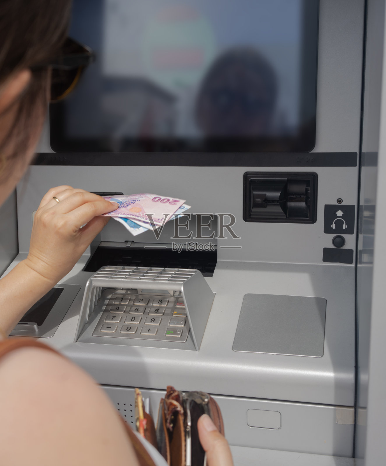 一名妇女在使用自动取款机，插入自动取款机上的信用卡。在自动取款机上取钱。照片摄影图片